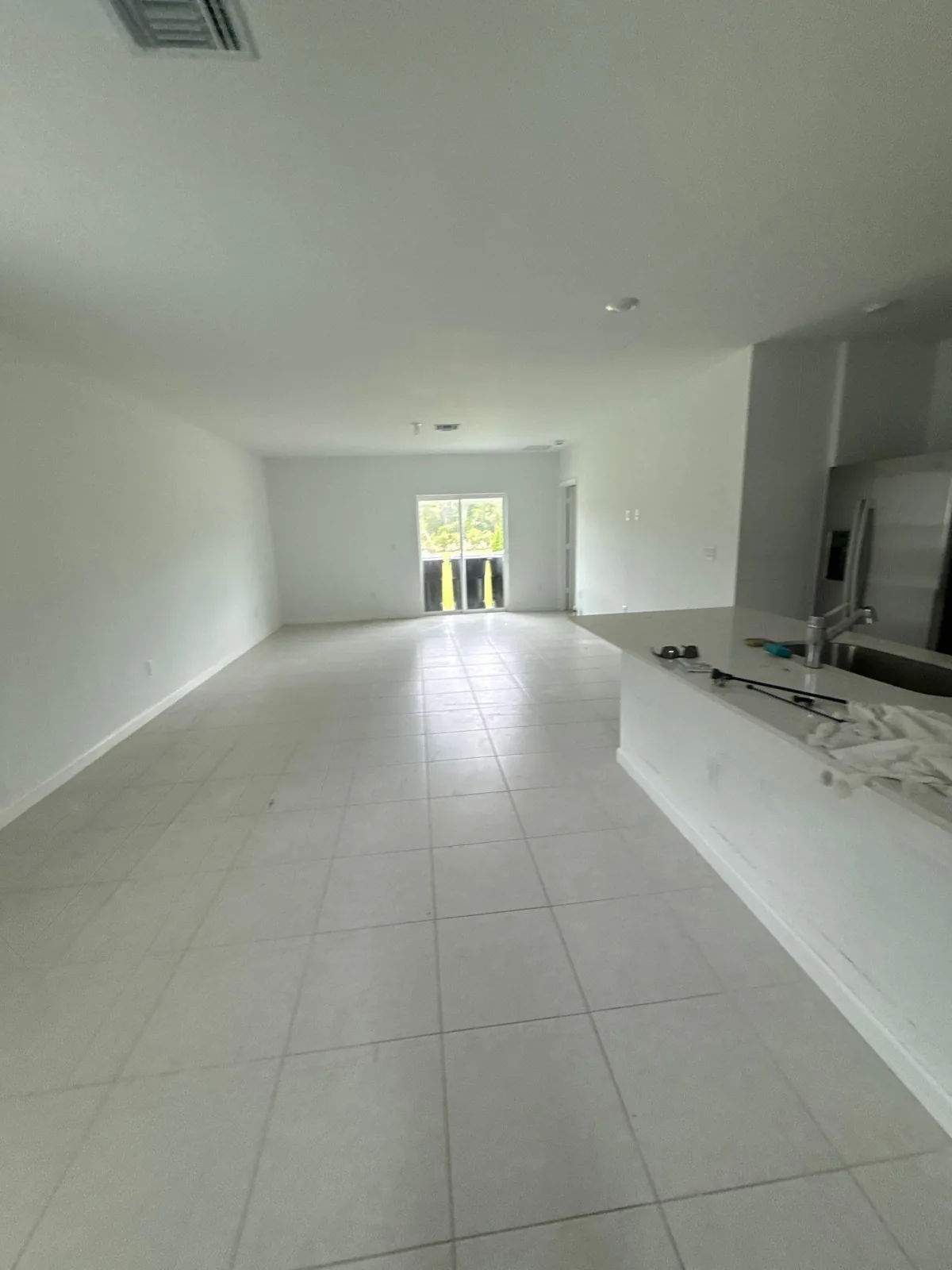 Interior Painting in Port Saint Lucie, Florida. Open-plan living area with white walls, tile flooring and glass doors at the far end.