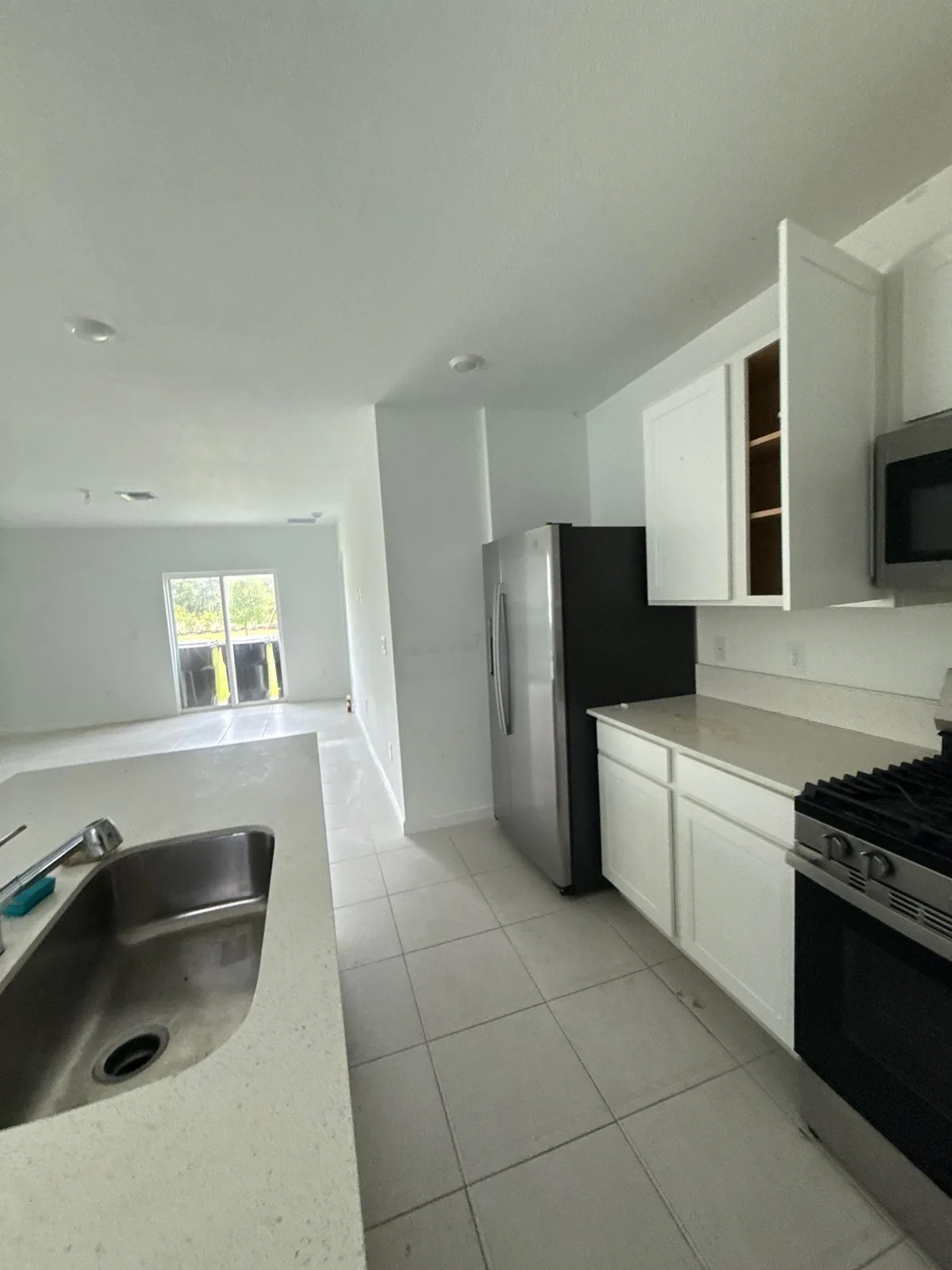 Interior Painting in Port Saint Lucie, Florida. Kitchen with white upper and lower cabinets, stainless refrigerator and range, tile floor and open living area beyond.