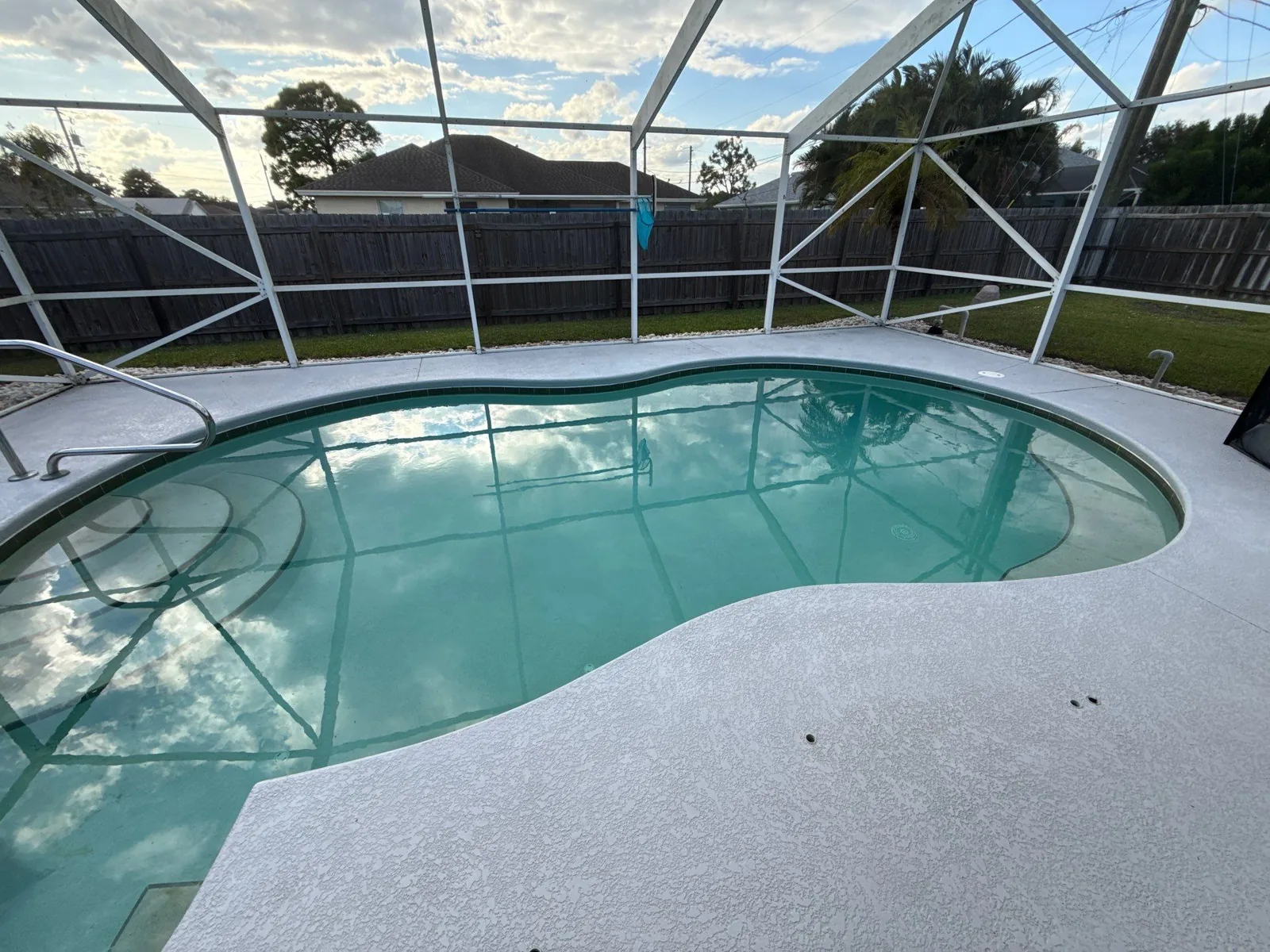 Pressure Washing in Port Saint Lucie, Florida. Screen-enclosed backyard swimming pool with clean light-grey textured concrete deck.