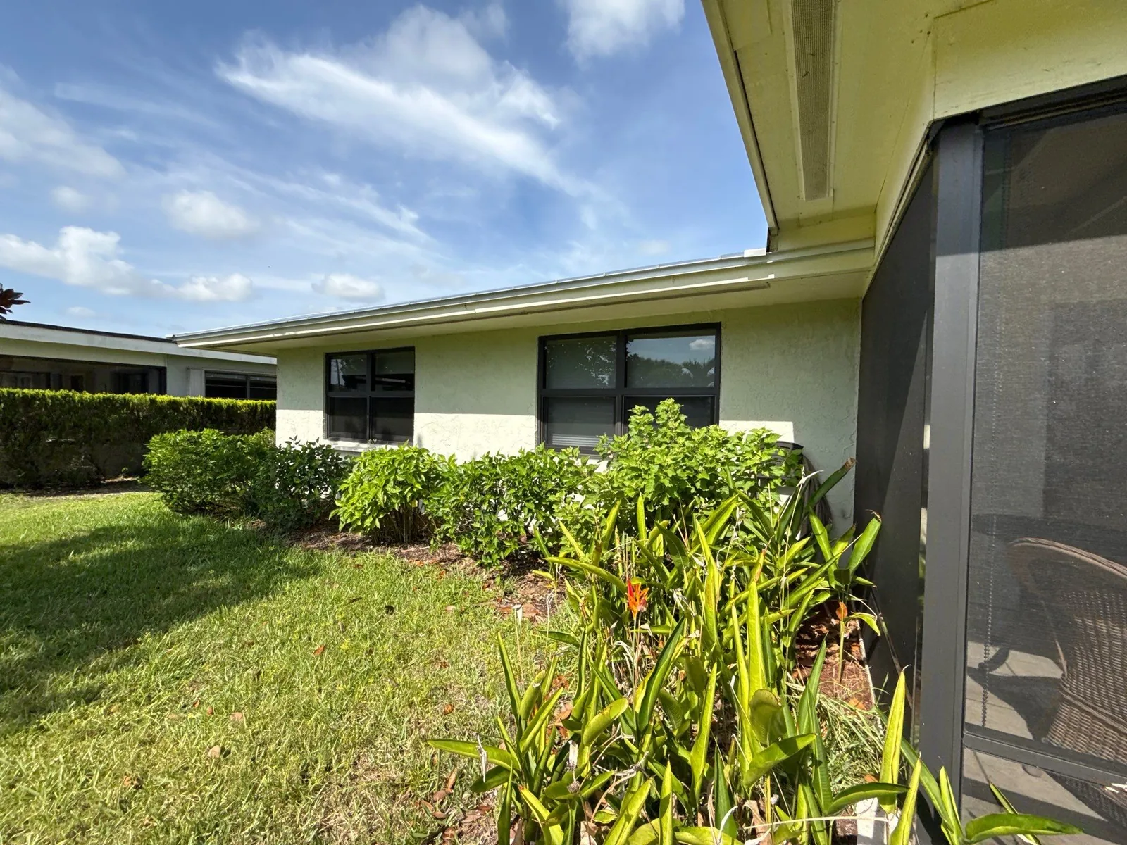 Exterior Painting in Port Salerno, Florida. Single-storey stucco home exterior painted light neutral with darker fascia and dark window frames, blue sky above.