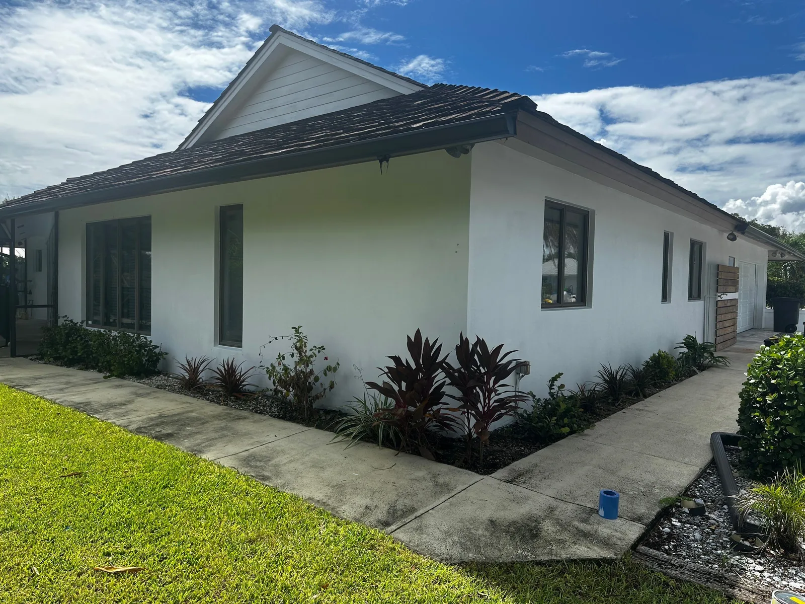 Exterior Painting in Port Salerno, Florida. Single-storey stucco house painted white with dark tile roof, landscaped bed of shrubs along the front walkway.