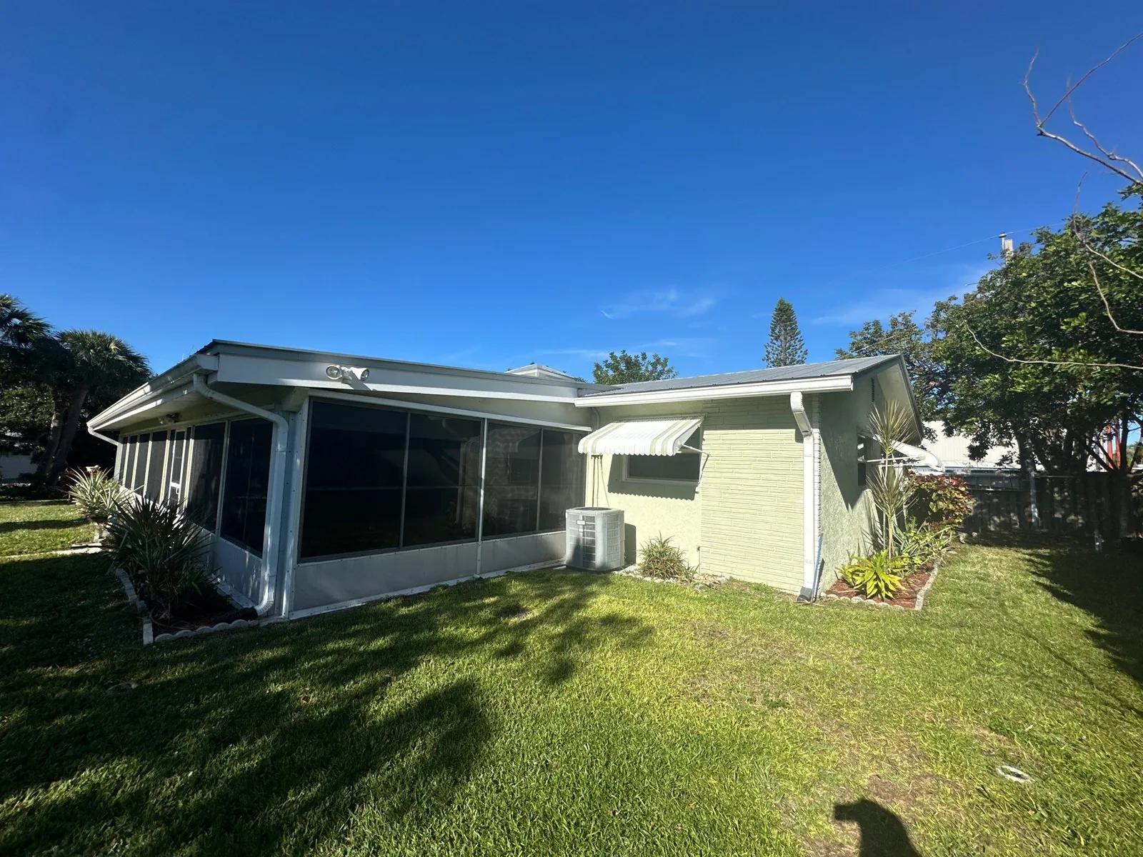 Exterior Painting in Port Salerno, Florida. Single-storey house exterior painted pale green with white trim and a screened porch, lawn in foreground.