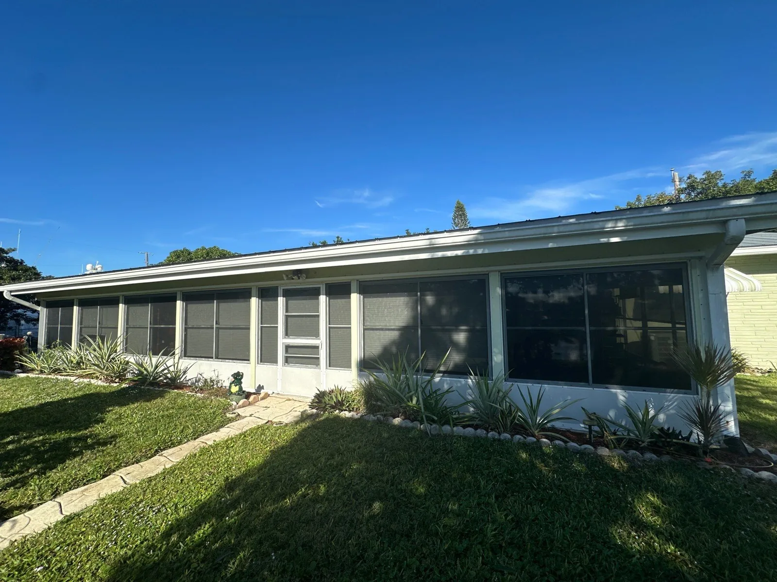 Exterior Painting in Port Salerno, Florida. Front elevation of a single-storey house painted pale green with white trim, screened windows and a lawn.