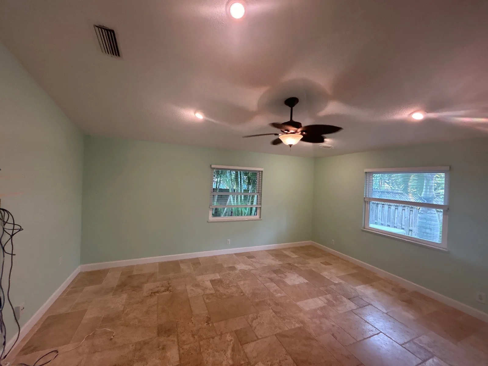Interior Painting in Port Salerno, Florida. Empty room with freshly painted pale green walls, white ceiling, ceiling fan and tile flooring.
