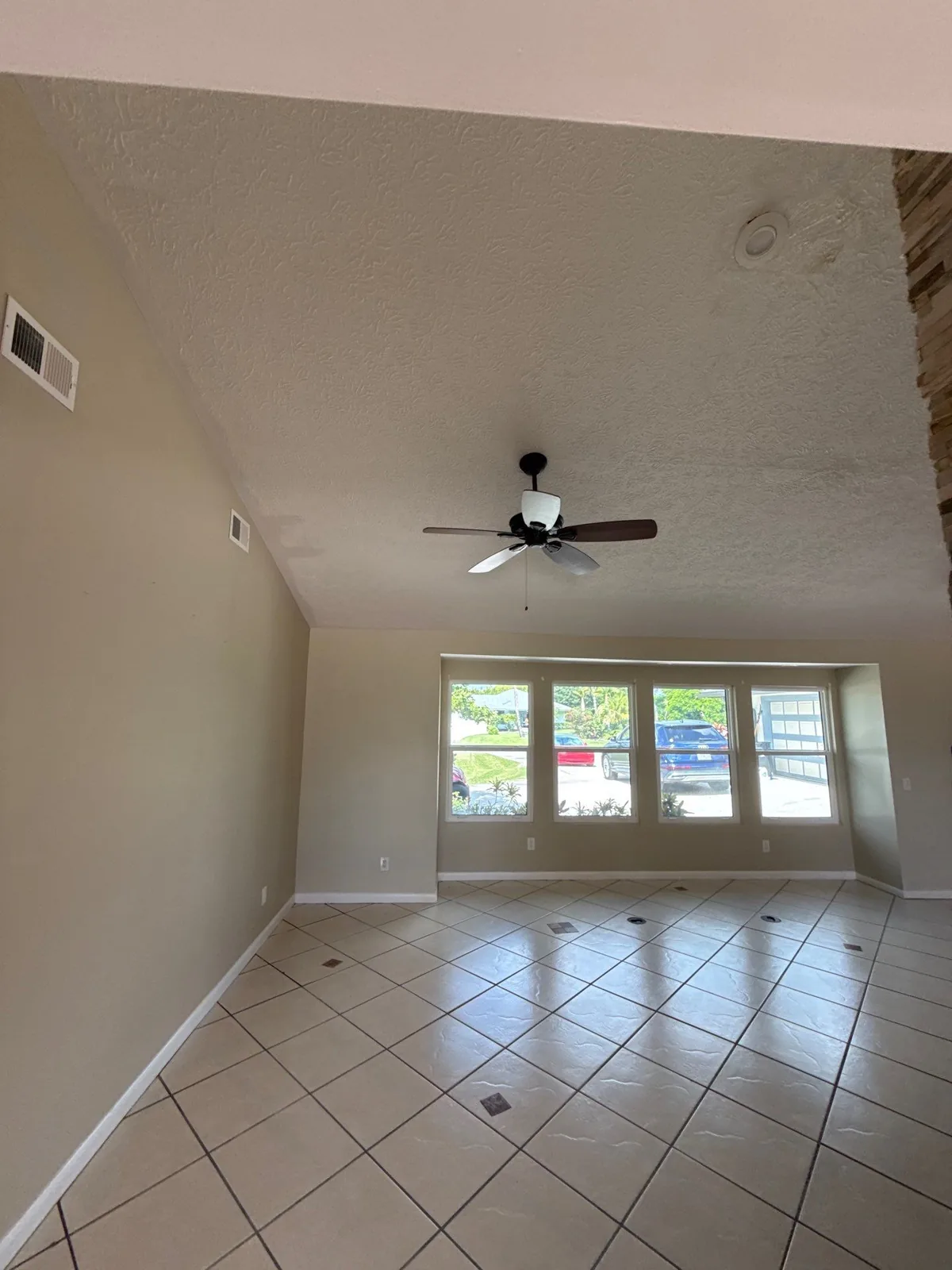Interior Painting in Port Salerno, Florida. Empty living room with vaulted ceiling, beige walls, white trim, bank of windows and tile floor.