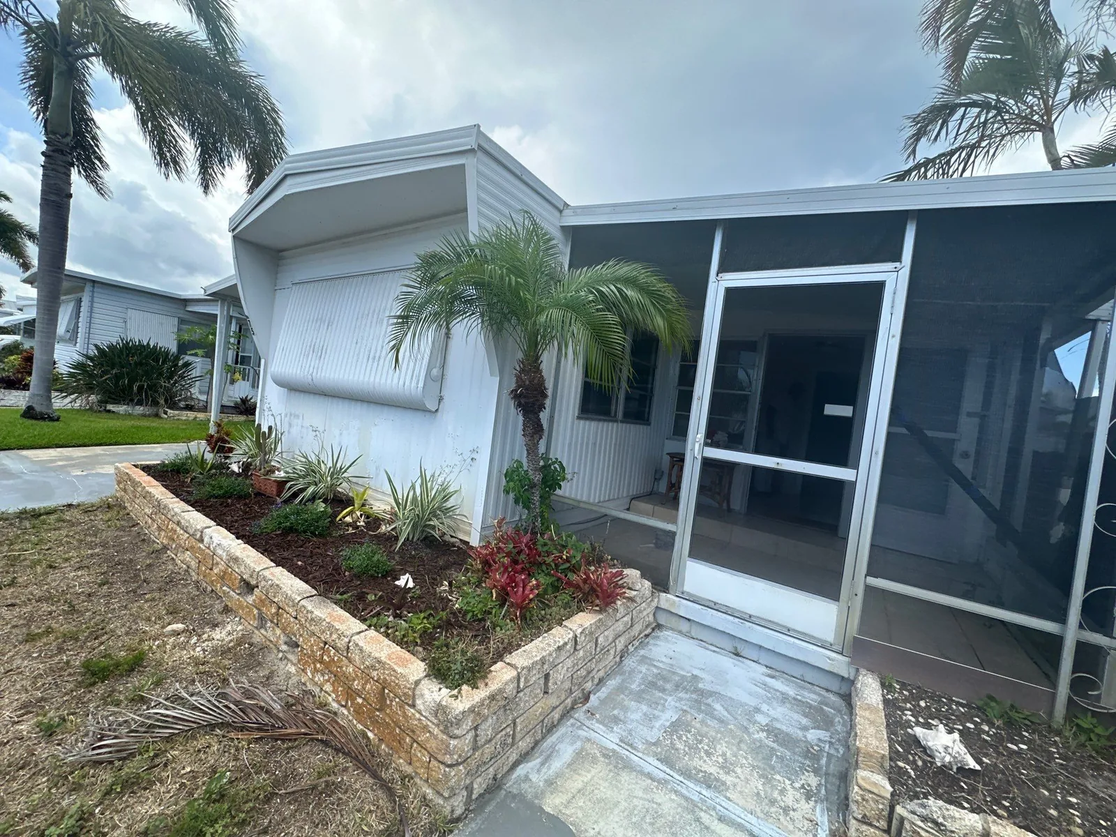 Pressure Washing in Port Salerno, Florida. Front entrance of a manufactured home with clean white siding, a screened porch door, awning and a brick planter with shrubs.