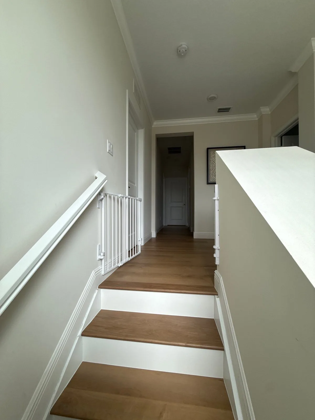 Interior Painting in Royal Palm Beach, Florida. Upstairs hallway and stairs with white walls, crown moulding, white painted banister and balusters, and wood-tread stairs.