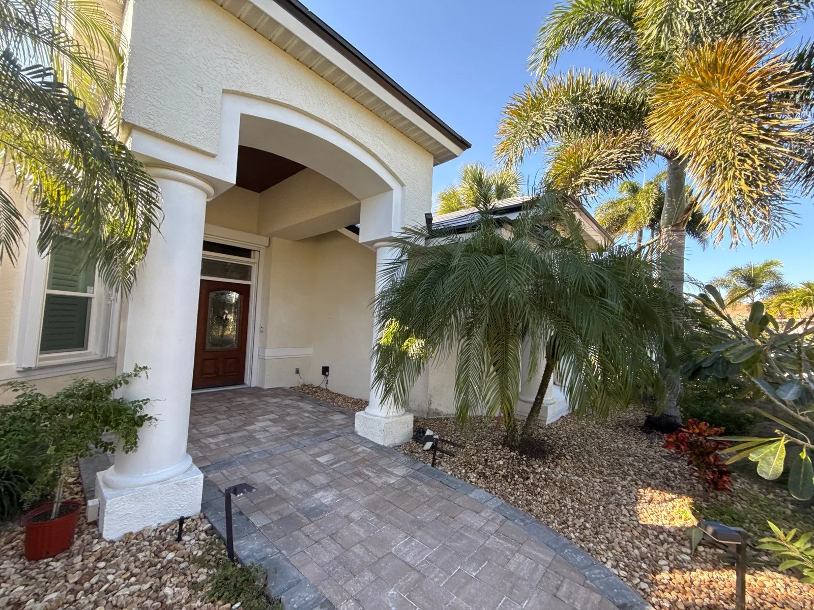 Exterior Painting in Satellite Beach, Florida. Arched front entry of a home with cream stucco, white columns, paver walkway and palms.