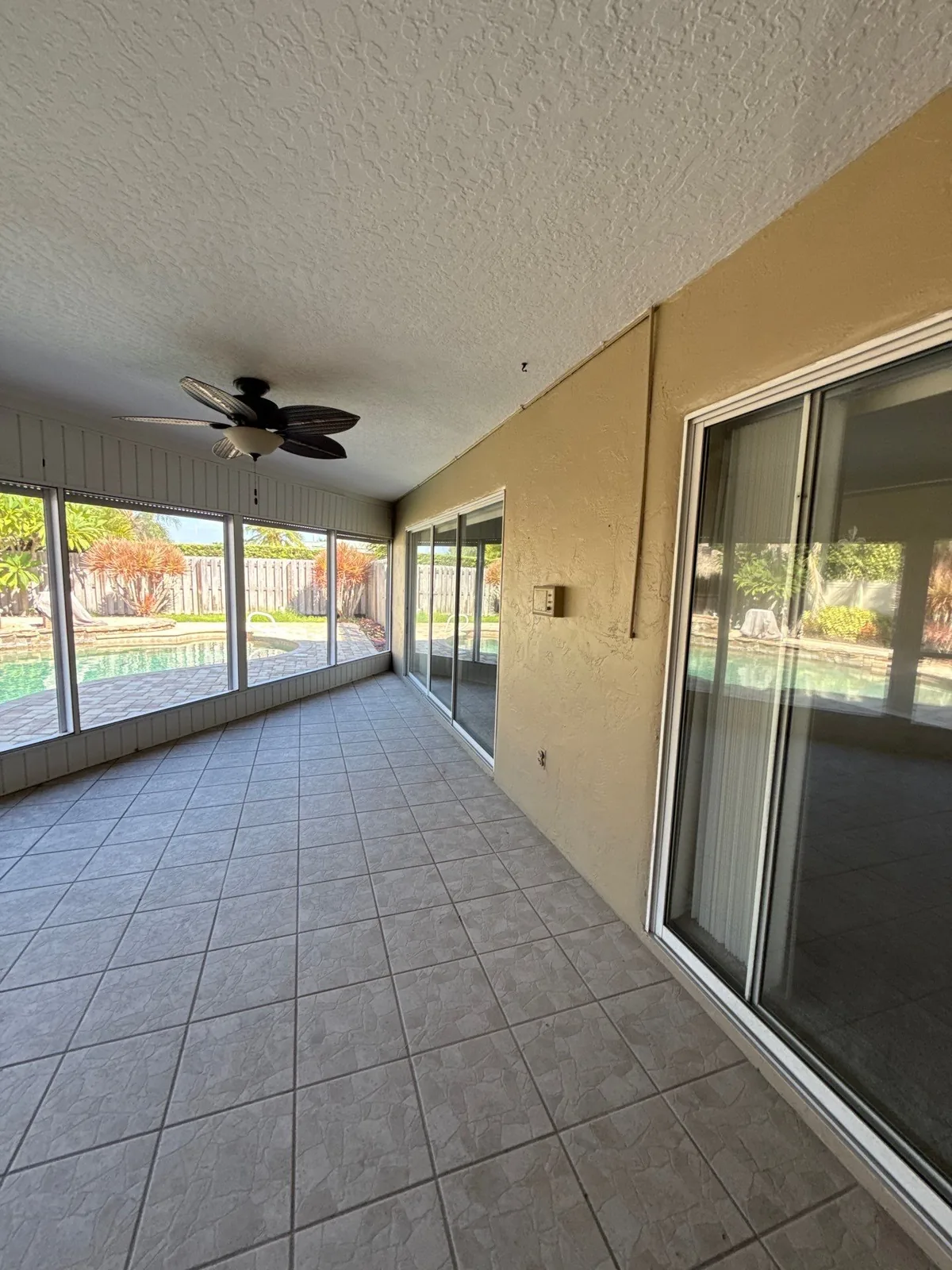 Exterior Painting in Satellite Beach, Florida. Covered screened lanai with tan painted stucco walls, textured ceiling, ceiling fan and tile floor.