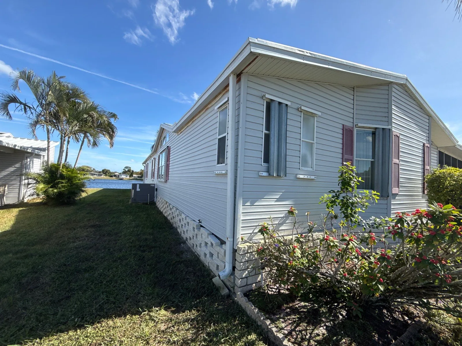 Exterior Painting in Sebastian, Florida. Side elevation of a single-storey home with white horizontal siding and mauve shutters, palm trees and a lake in the background.