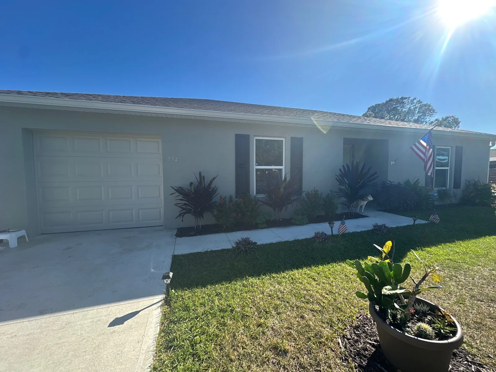 Exterior Painting in Sebastian, Florida. Single-storey stucco house exterior, pale walls with dark window shutters and a white garage door, front lawn and driveway.
