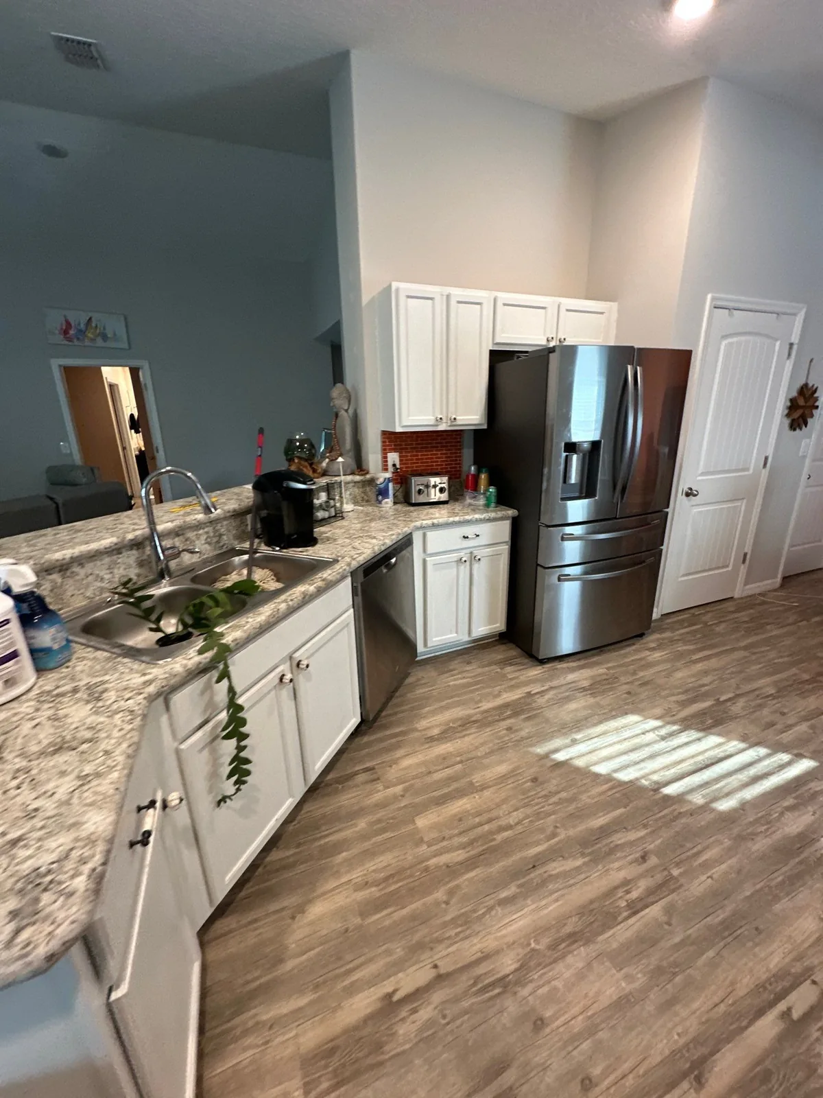 Interior Painting in Sebastian, Florida. Kitchen with white cabinets, stone countertops and stainless refrigerator, wood-look plank flooring.