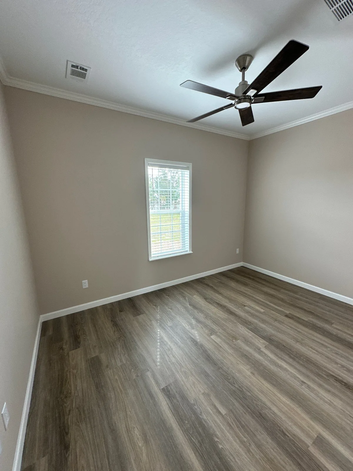 Interior Painting in Sebastian, Florida. Empty bedroom with beige walls, white crown moulding and baseboards, ceiling fan and a single window with blinds.