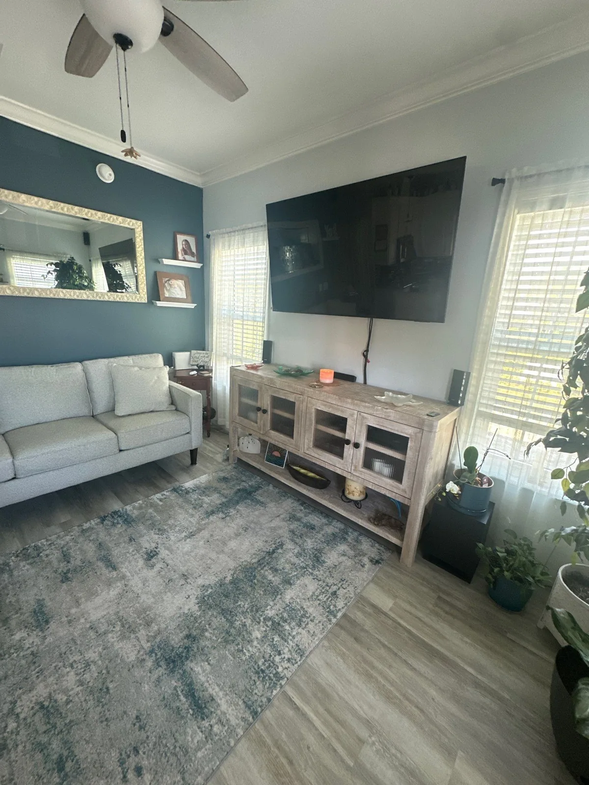 Interior Painting in Sebastian, Florida. Living room with a dark teal accent wall, white ceiling and trim, ceiling fan, sofa and media console.