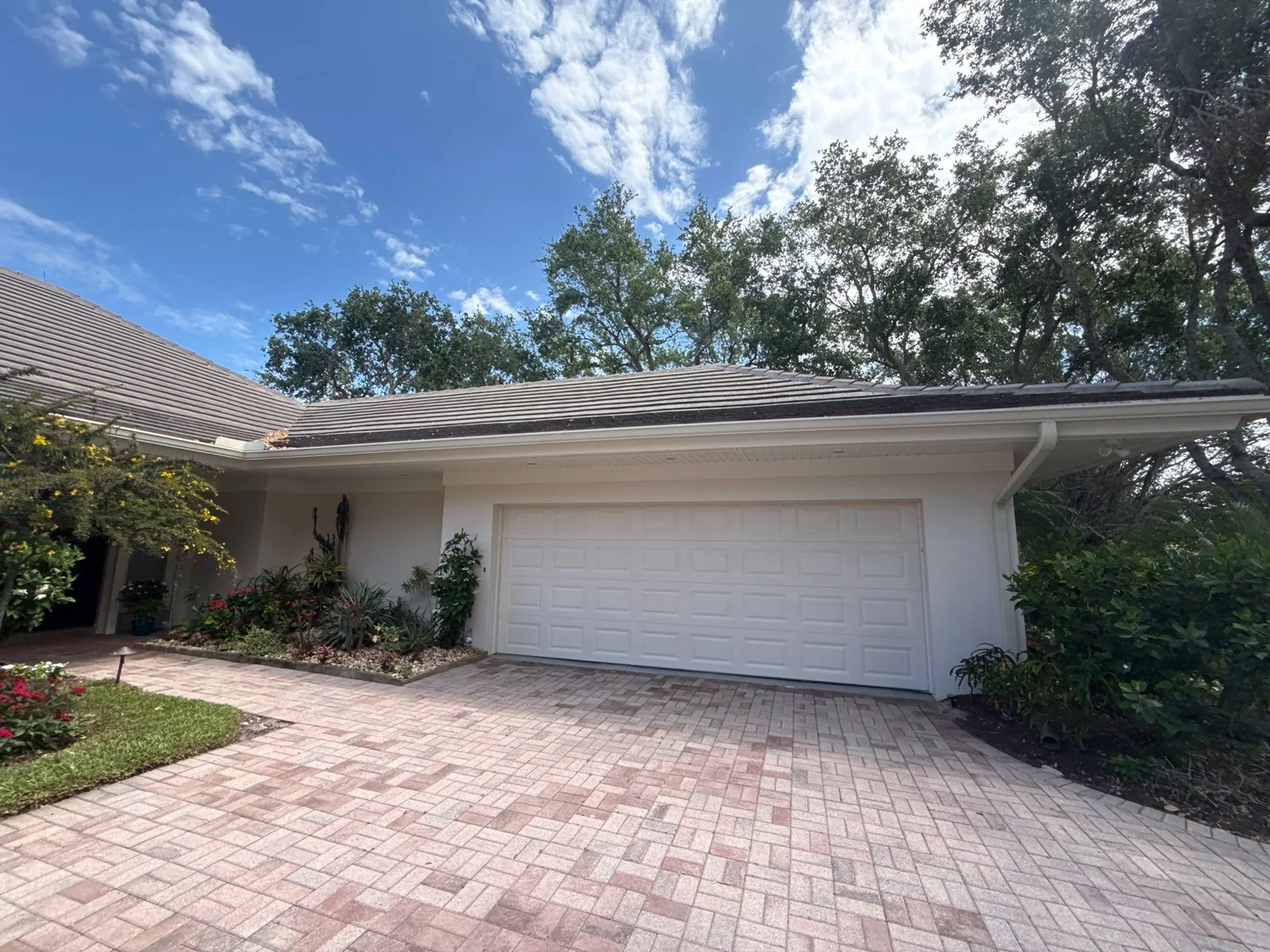 Exterior Painting in South Beach, Florida. Single-storey home exterior painted white with a tile roof, white two-car garage door and a brick paver driveway.
