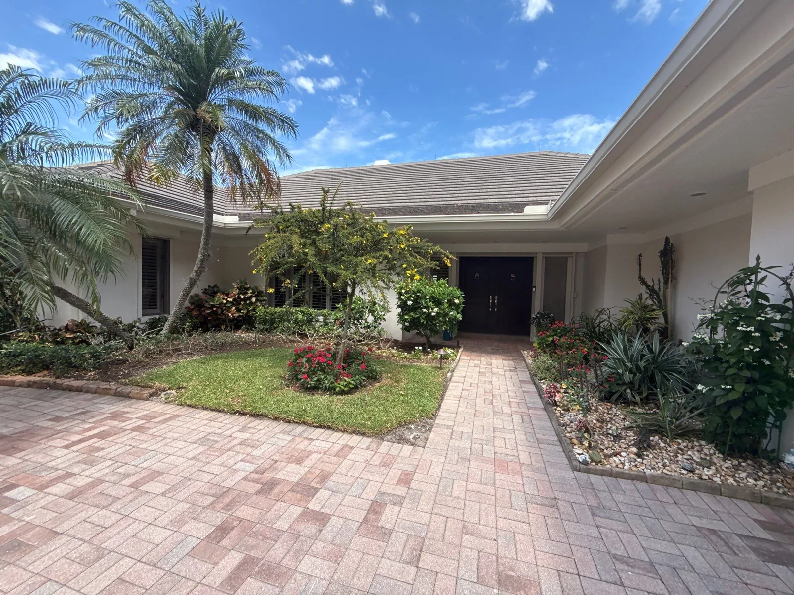 Exterior Painting in South Beach, Florida. Front entrance of a single-storey home with off-white painted stucco, dark double front door, brick paver walkway and planted beds.