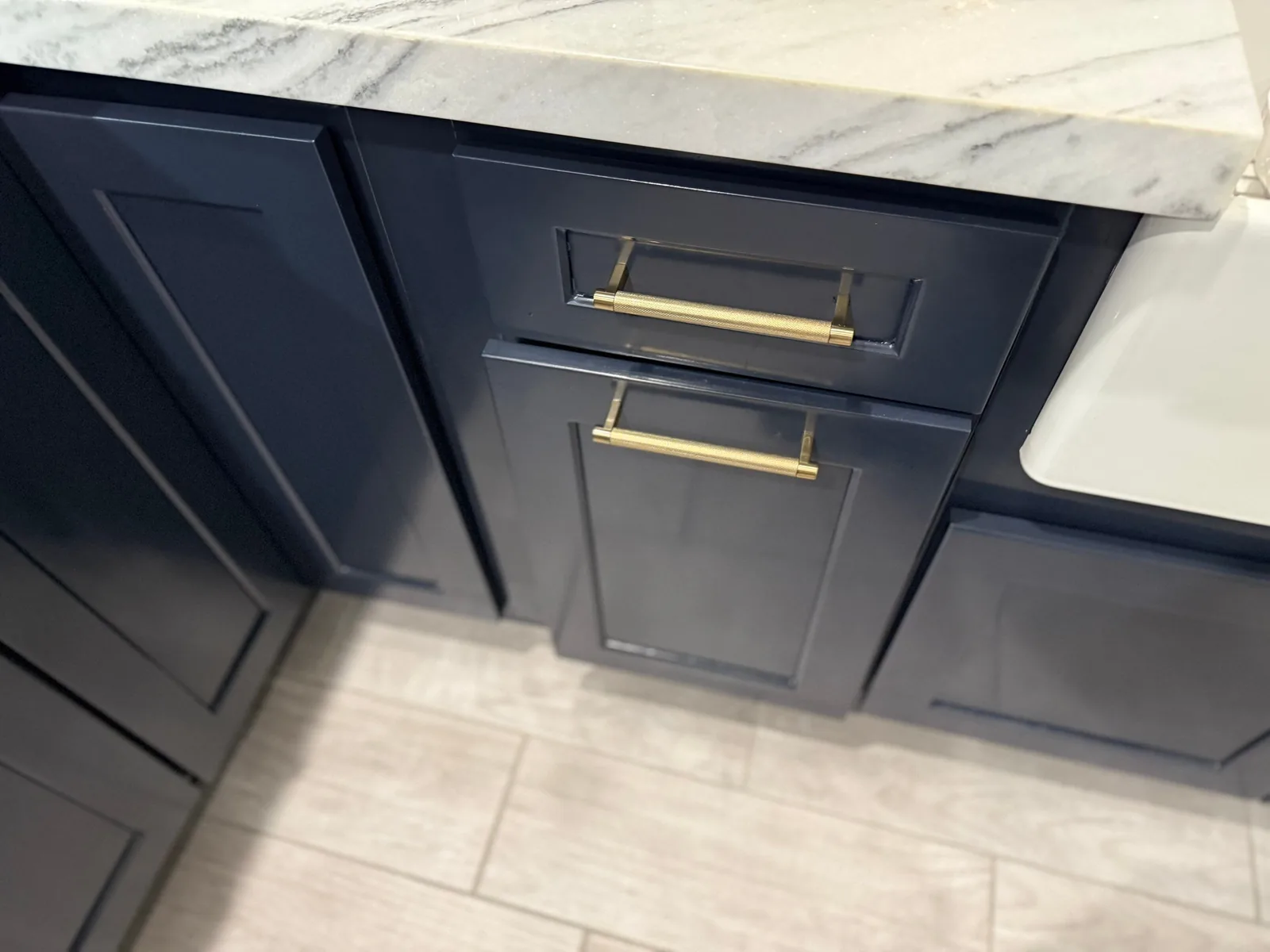 Cabinet Refinishing in Stuart, Florida. Navy blue cabinet drawers with long brass pulls beside a white apron-front sink and marble-look counter.