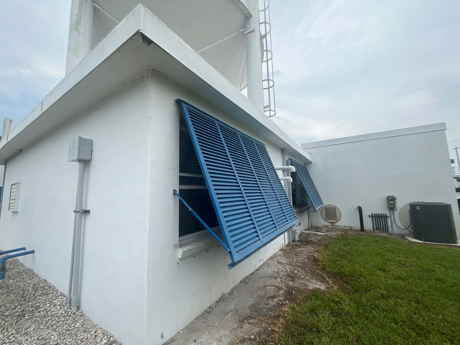 Commercial Painting in Stuart, Florida. White painted concrete utility building with blue louvered awning vents and tank behind.