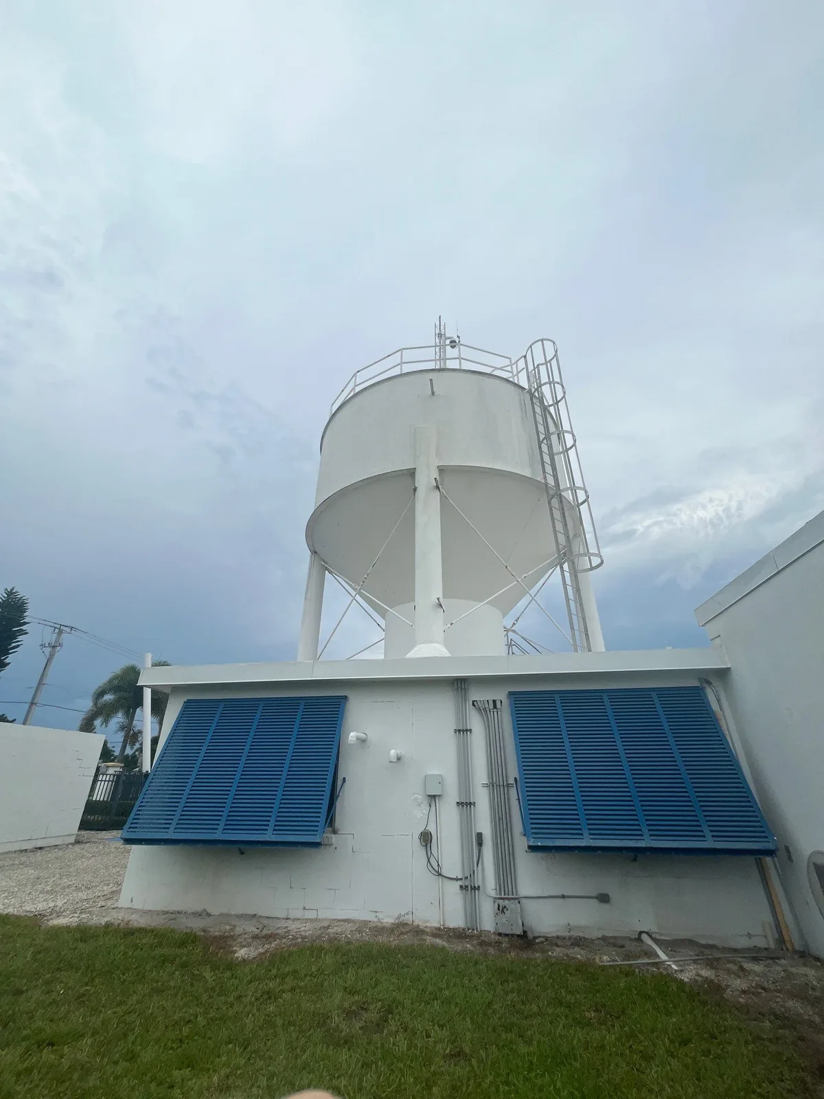 Commercial Painting in Stuart, Florida. White elevated storage tank above a white painted building with blue louvered vents, blue sky behind.