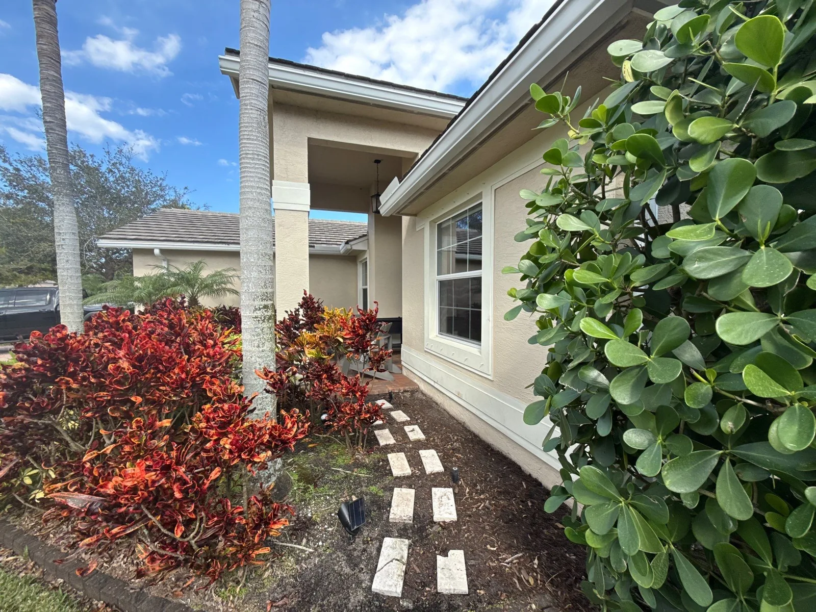 Exterior Painting in Stuart, Florida. Side elevation of a single-storey home, beige stucco with white trim, paver walkway and shrub bed.