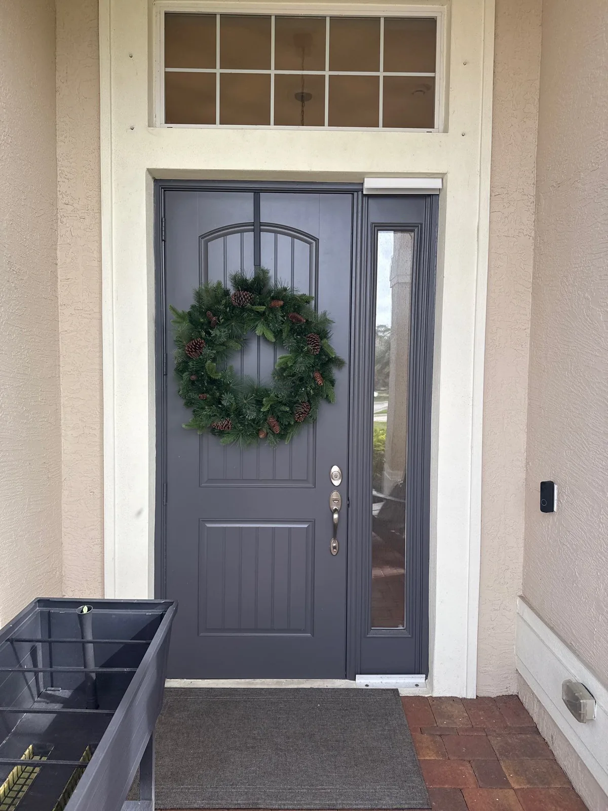 Exterior Painting in Stuart, Florida. Grey painted front entry door with sidelight and transom window, wreath hung on the door.