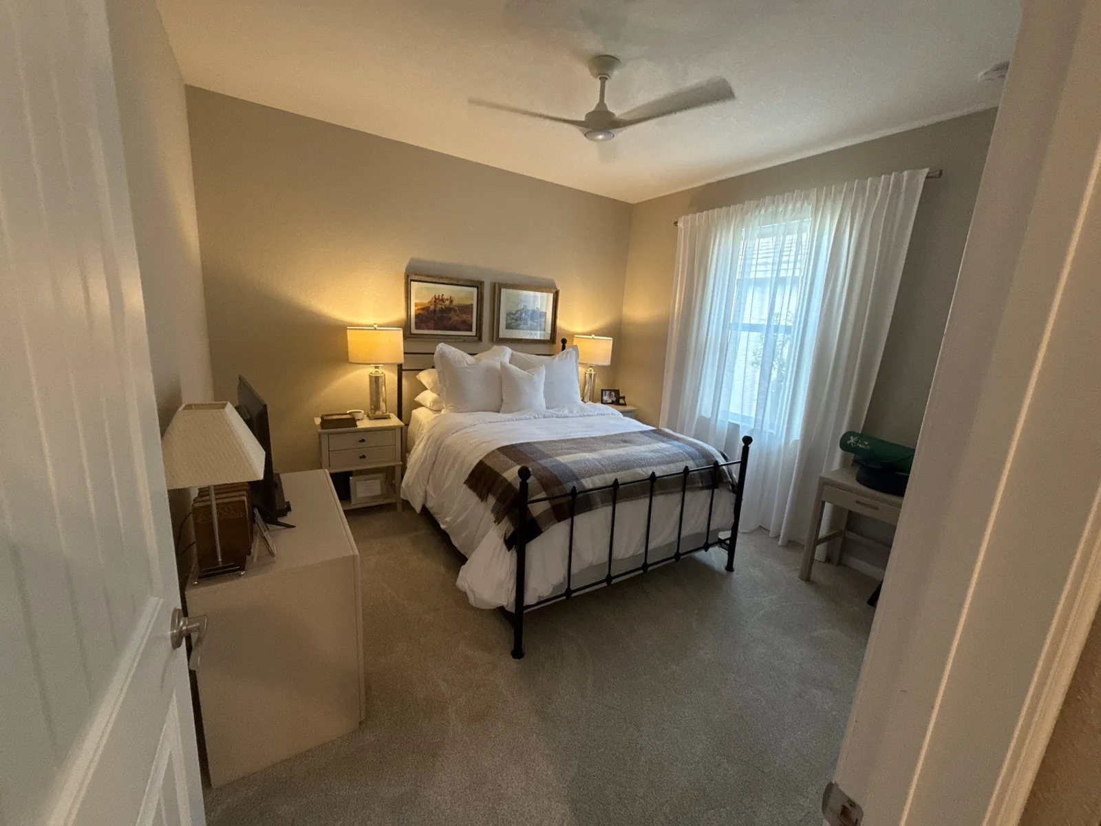 Interior Painting in Stuart, Florida. Finished bedroom with greige painted walls and white ceiling, metal-frame bed, two lit bedside lamps and a ceiling fan.