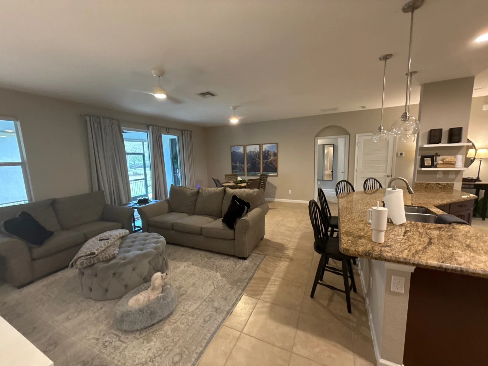 Interior Painting in Stuart, Florida. Open-plan living room and kitchen with light neutral painted walls, sectional seating, granite breakfast bar with pendant lights and tile flooring.