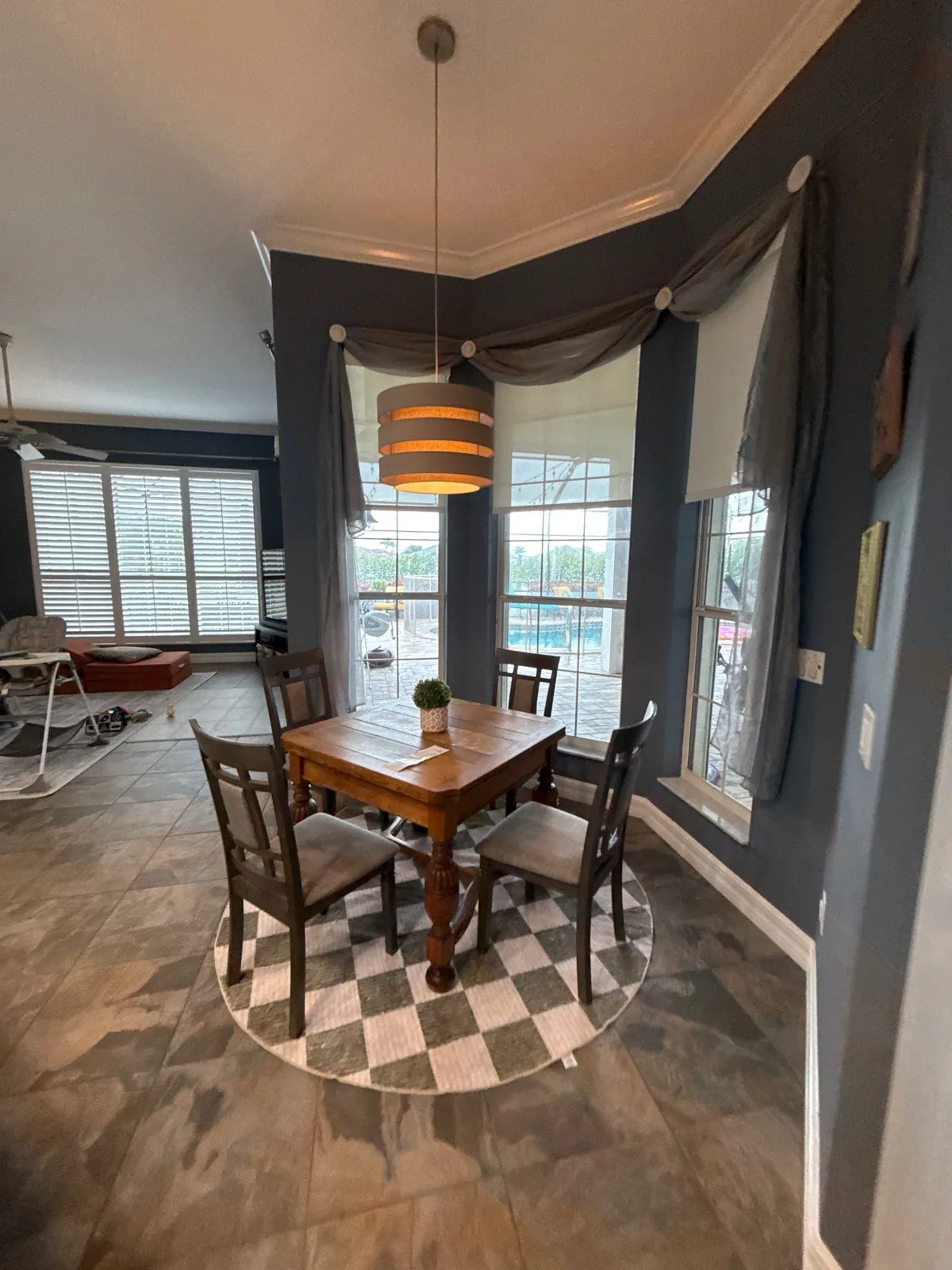 Interior Painting in Suntree, Florida. Breakfast nook with dark blue-grey walls, white crown moulding, wood table and chairs and a pendant light.