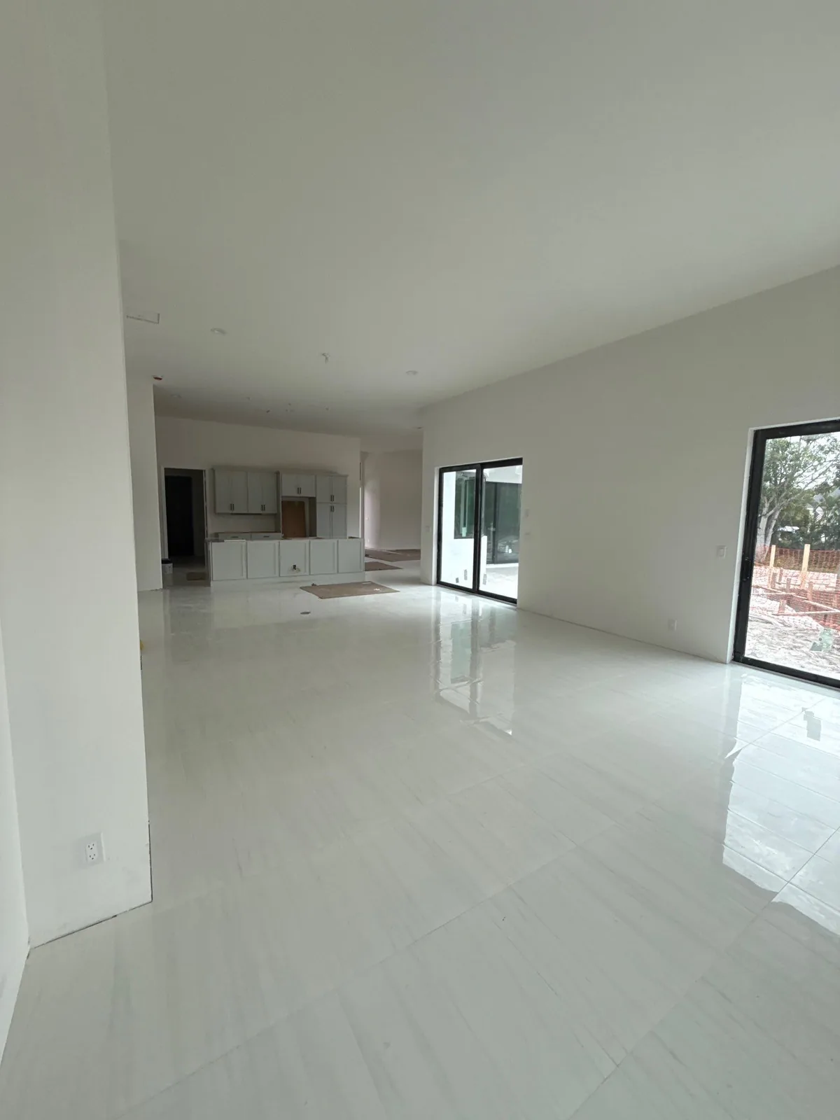 Interior Painting in The Acreage, Florida. Open-plan living area with white walls and ceiling, glossy white tile floor, sliding glass doors and a kitchen with white cabinets in the background.