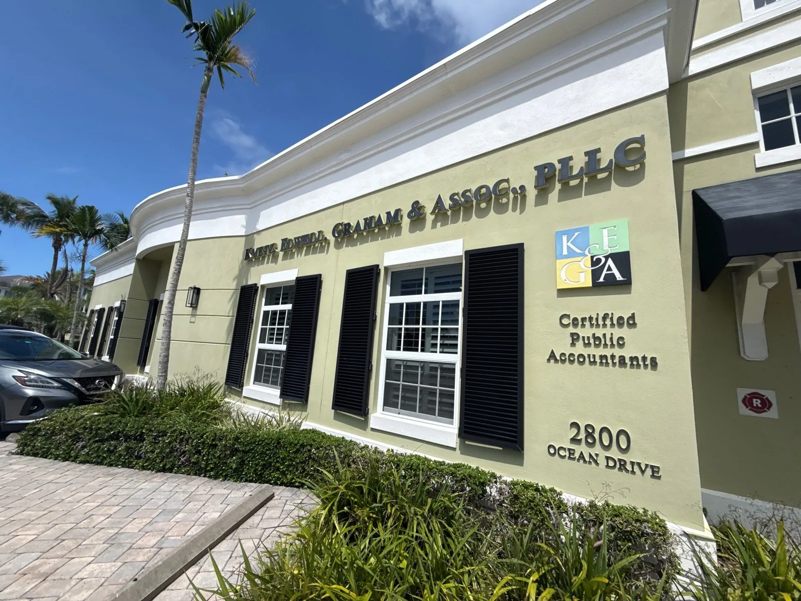 Commercial Painting in Vero Beach, Florida. Single-storey commercial office building exterior, pale olive stucco with white trim, black shutters and raised lettering signage.