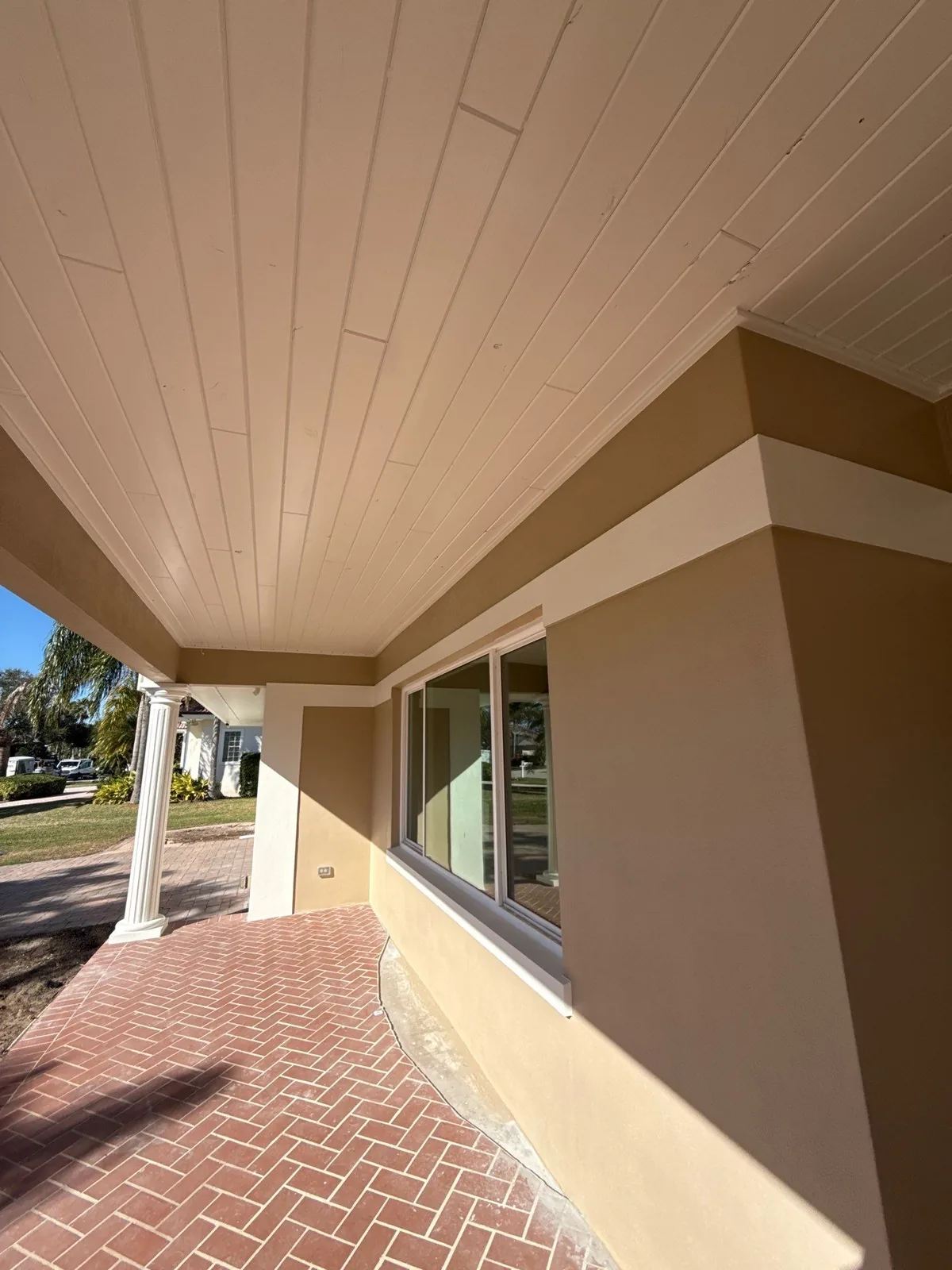 Exterior Painting in Vero Beach, Florida. Covered front porch with a painted tongue-and-groove ceiling, tan stucco walls with white trim and a brick paver walkway.