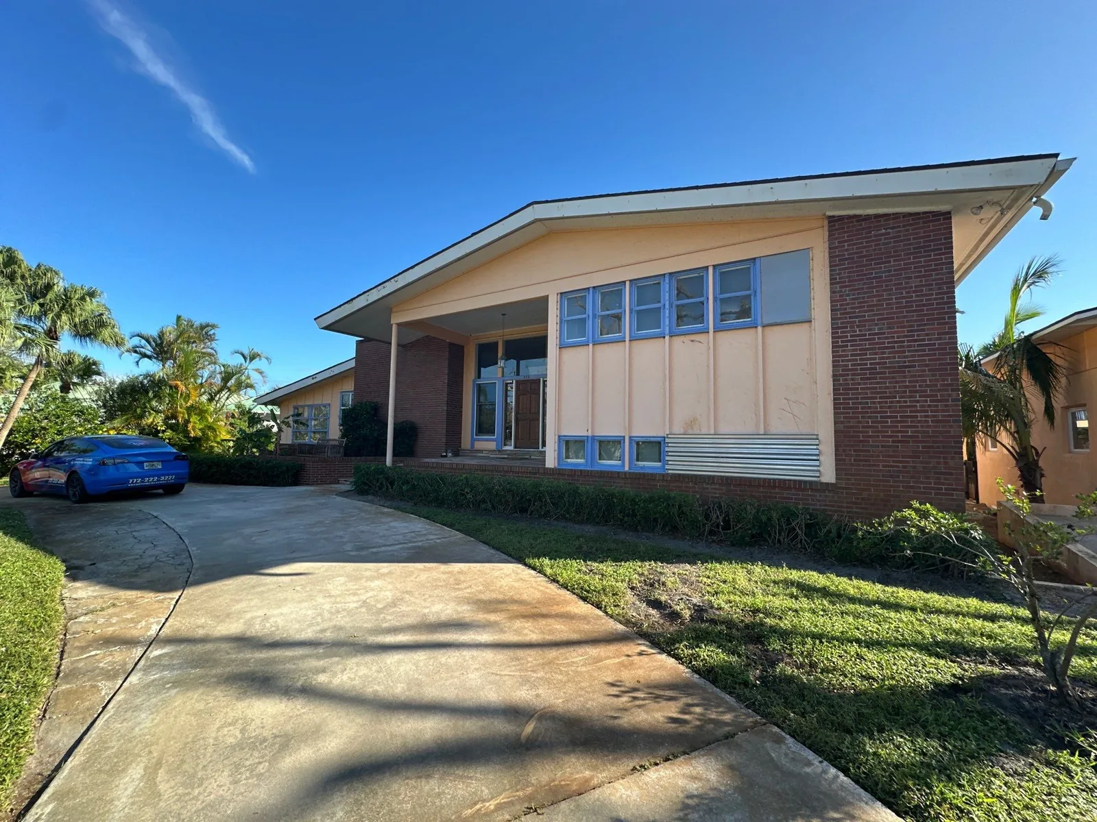 Exterior Painting in Vero Beach, Florida. Single-storey mid-century home with brick facade, peach painted wall panels and clerestory windows, concrete driveway.