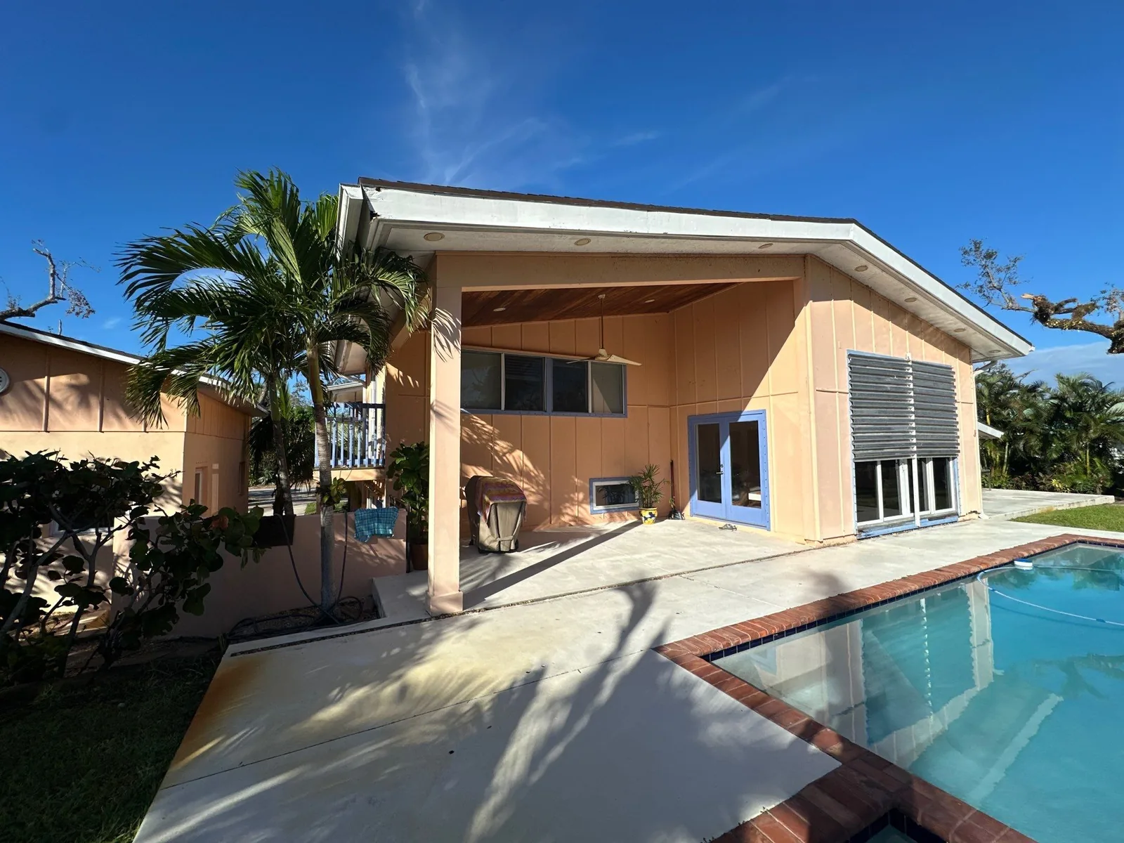 Exterior Painting in Vero Beach, Florida. Rear elevation of a single-storey home with peach painted walls, white fascia and covered patio, beside a swimming pool under clear sky.