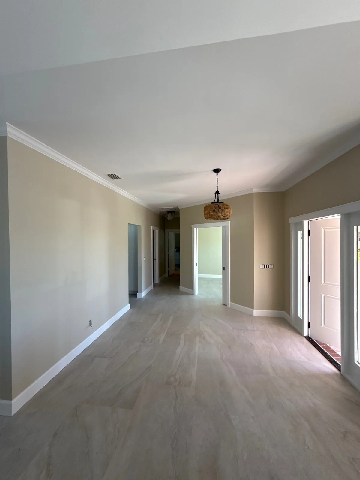 Interior Painting in Vero Beach, Florida. Open living area with beige walls, white crown moulding and baseboards, white front door and grey tile flooring.