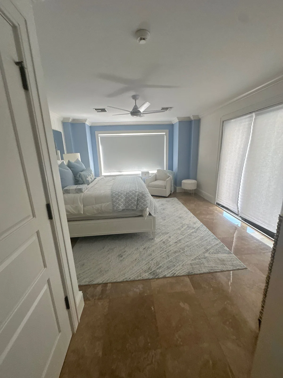 Interior Painting in Vero Beach, Florida. Bedroom with light blue walls, white ceiling and trim, made bed and ceiling fan.