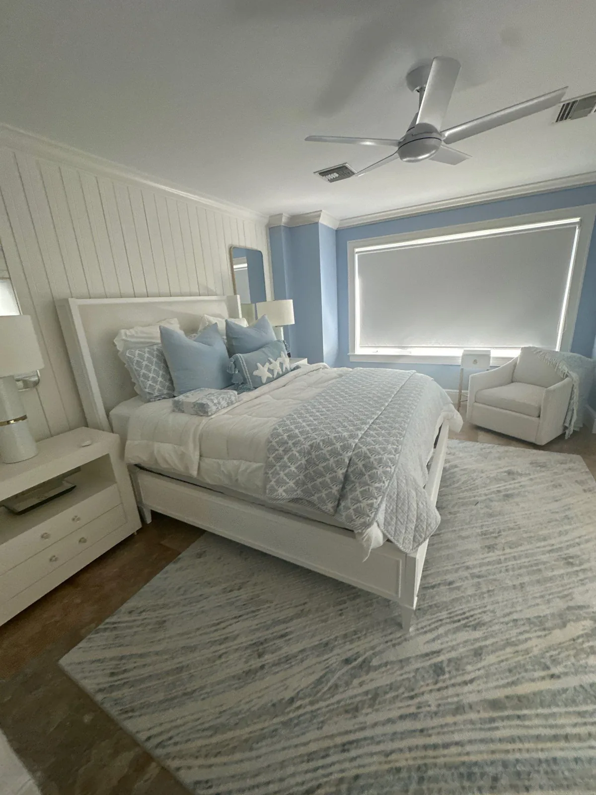 Interior Painting in Vero Beach, Florida. Bedroom with light blue accent wall, white vertical plank wall, white ceiling fan and made bed.