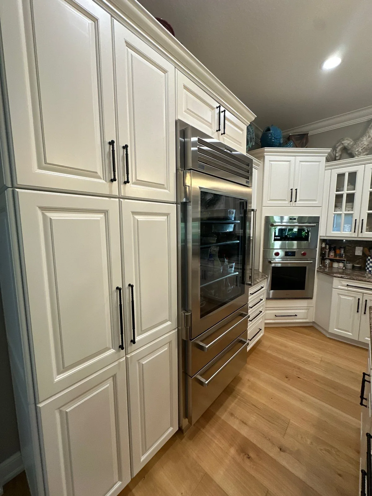 Cabinet Refinishing in Wabasso Beach, Florida. Run of white raised-panel kitchen cabinets with panelled refrigerator front and stainless wall ovens.