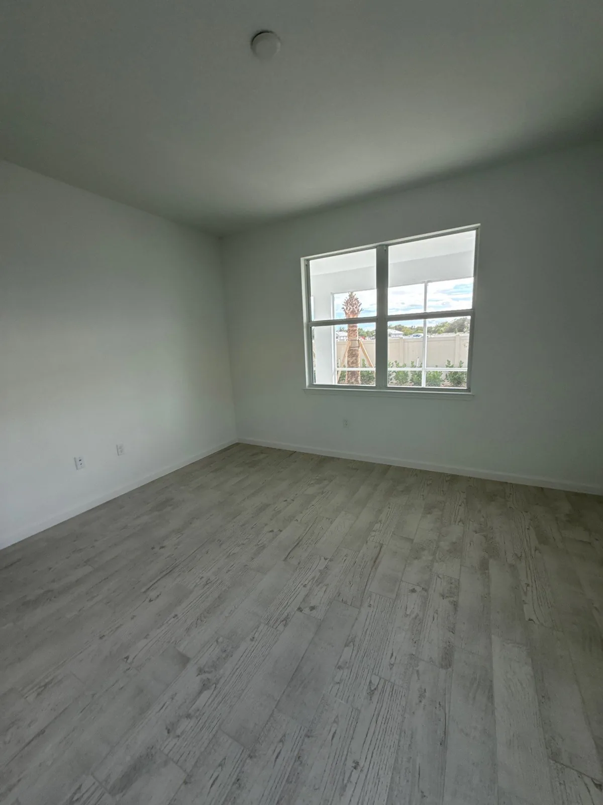 Interior Painting in Wabasso, Florida. Empty bedroom with white walls and smooth ceiling, single window and grey plank flooring.