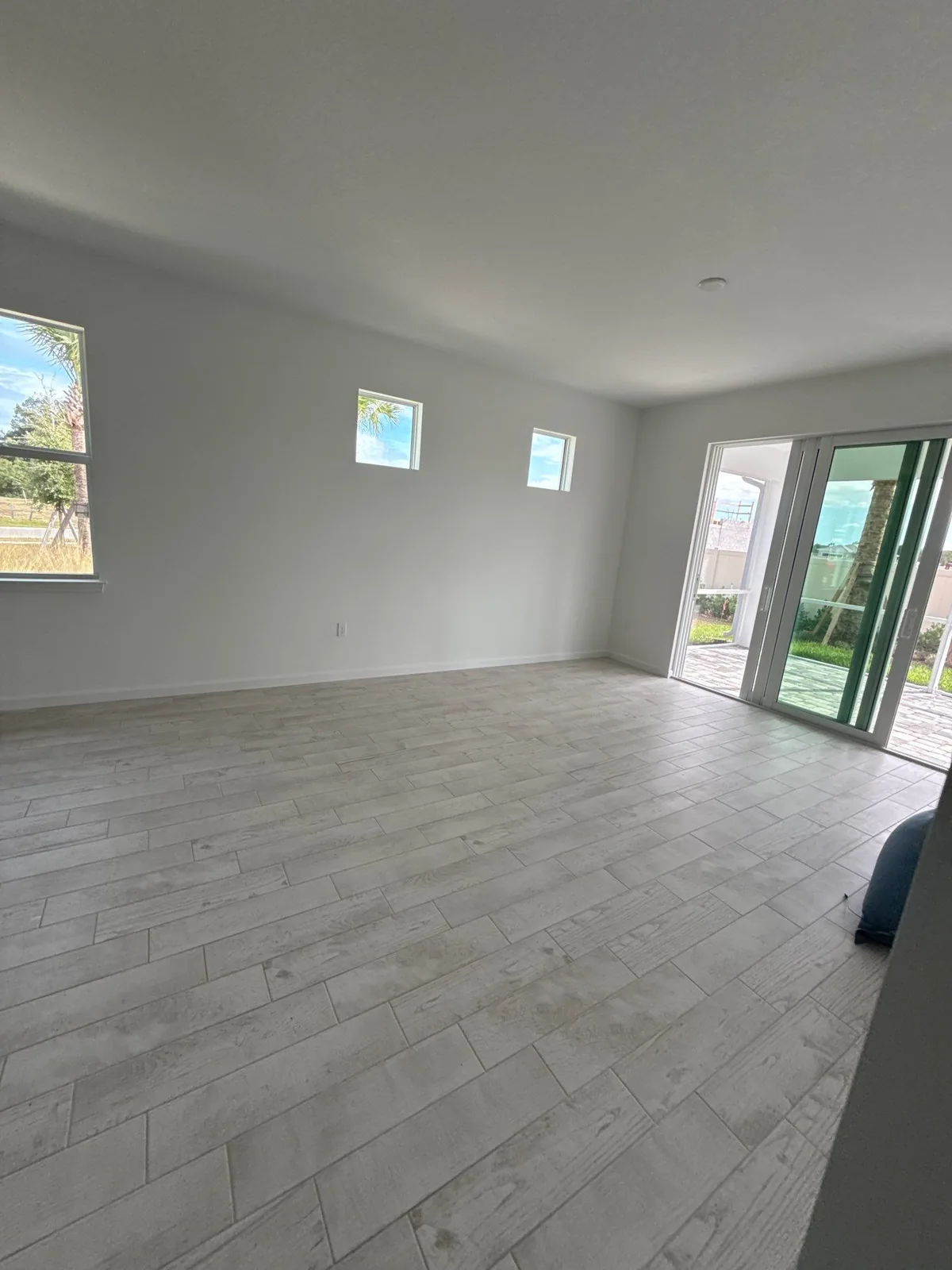 Interior Painting in Wabasso, Florida. Large empty living area with white walls, sliding glass doors and light plank tile flooring.