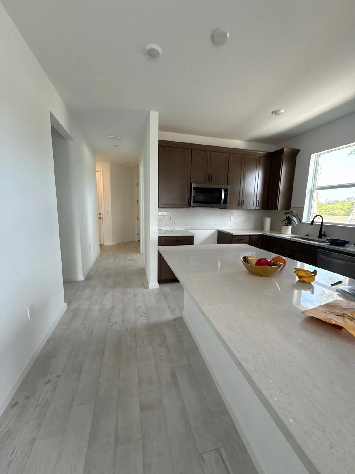 Interior Painting in Wabasso, Florida. Open-plan kitchen and hallway with white walls and ceiling, dark brown cabinets and a white stone island.