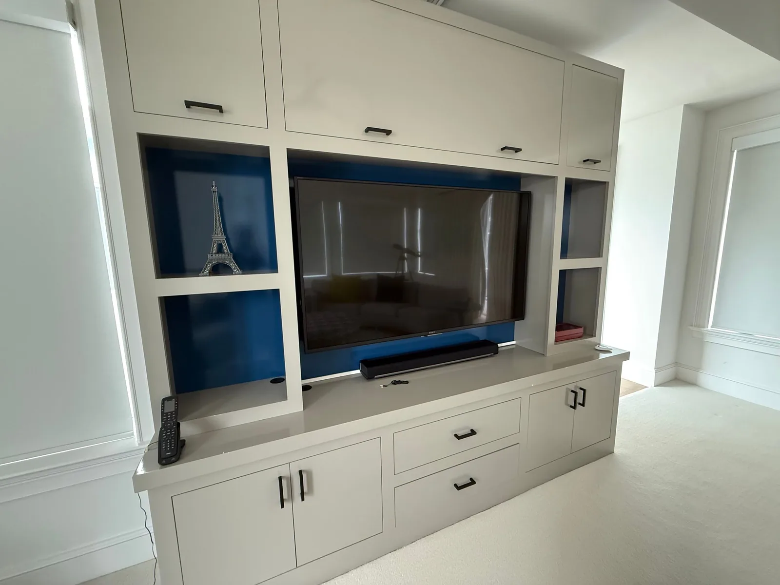 Cabinet Refinishing in Wellington, Florida. Built-in entertainment wall painted white with blue-painted open niches, wall-mounted television, drawers and cabinet doors with black bar pulls.