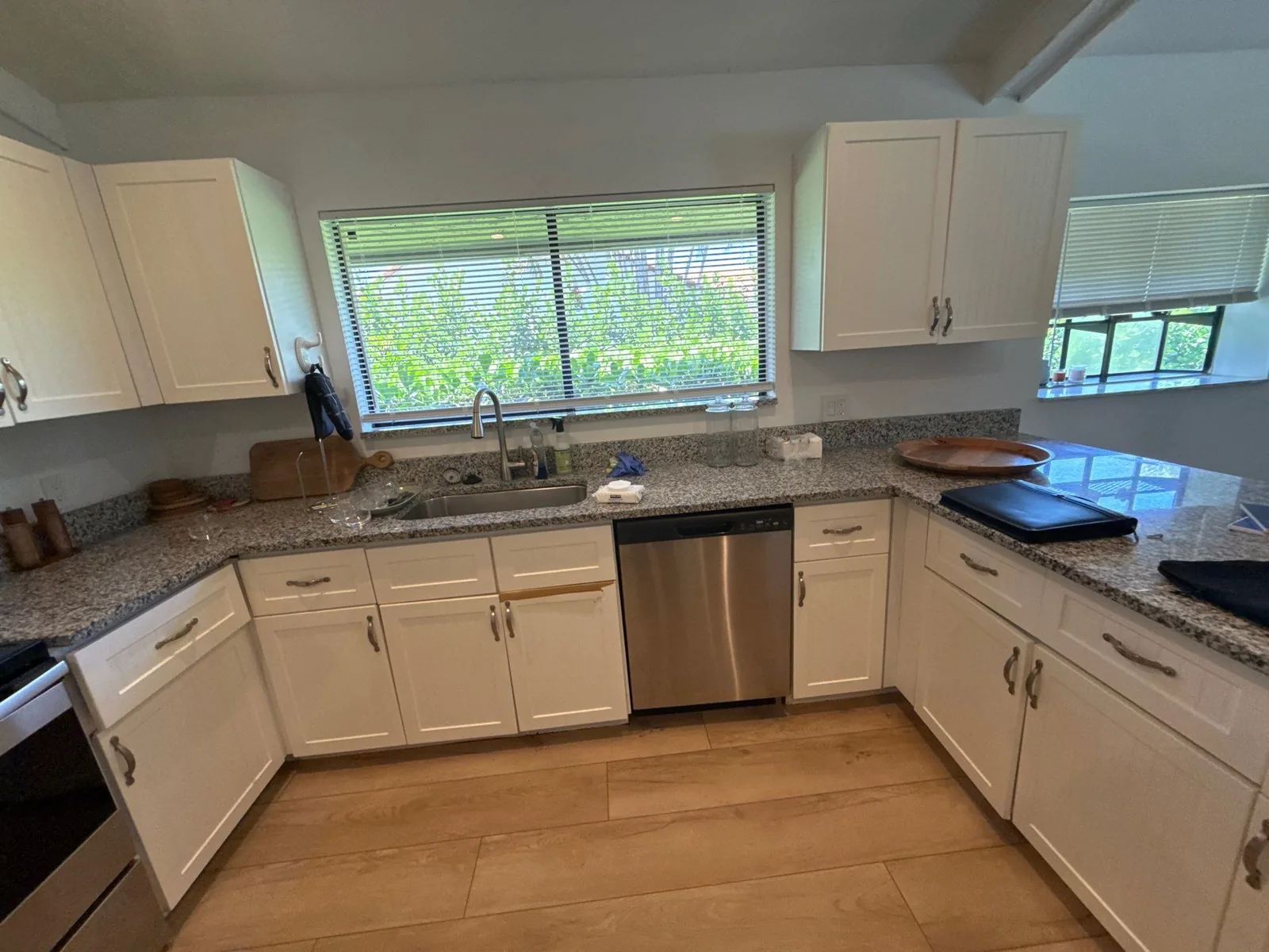Interior Painting in Wellington, Florida. L-shaped kitchen with white cabinets, granite countertops, window over the sink and stainless dishwasher.