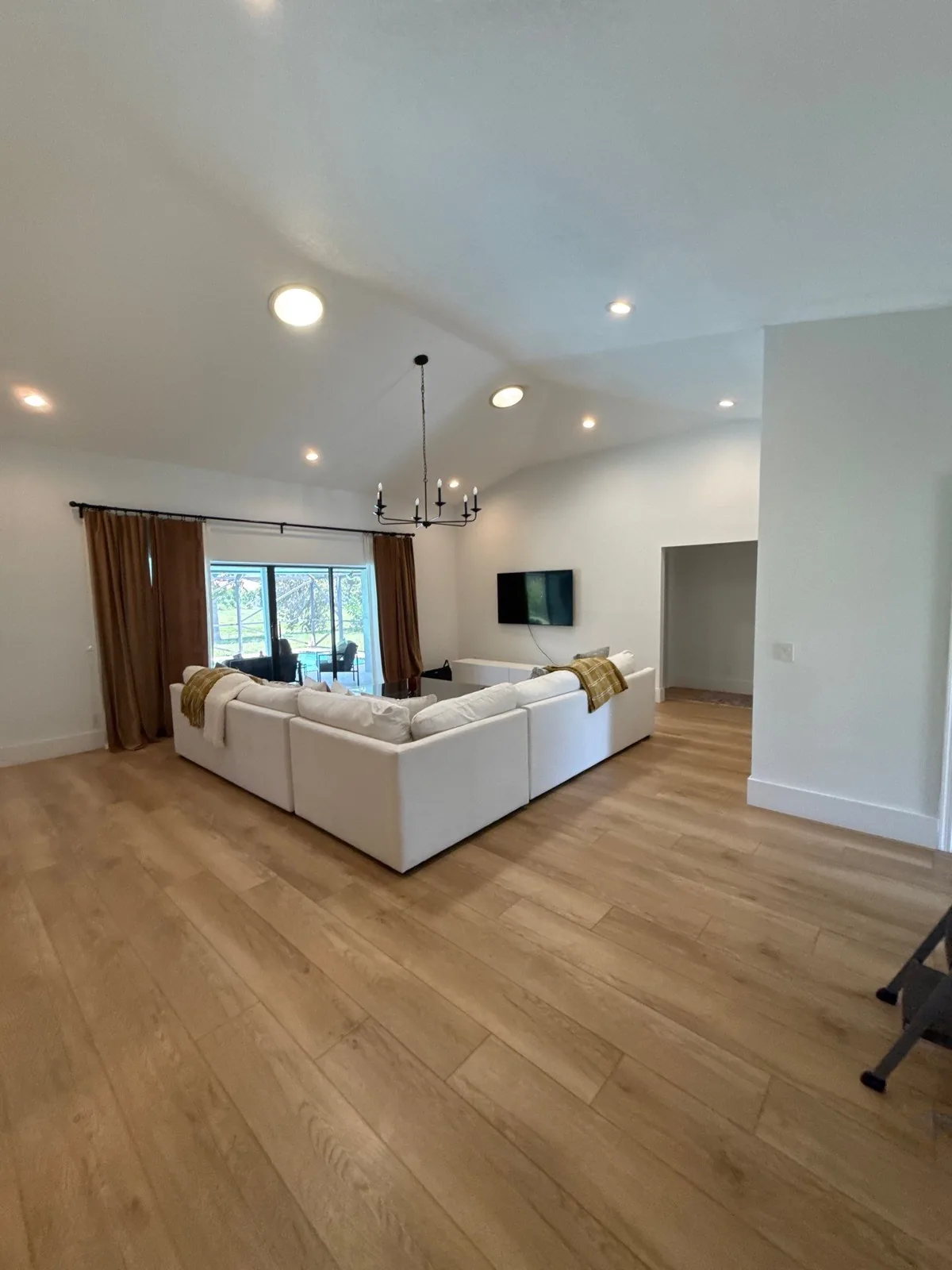 Interior Painting in Wellington, Florida. Open living room with vaulted white ceiling, white walls, recessed lighting, sectional sofa and light wood flooring.