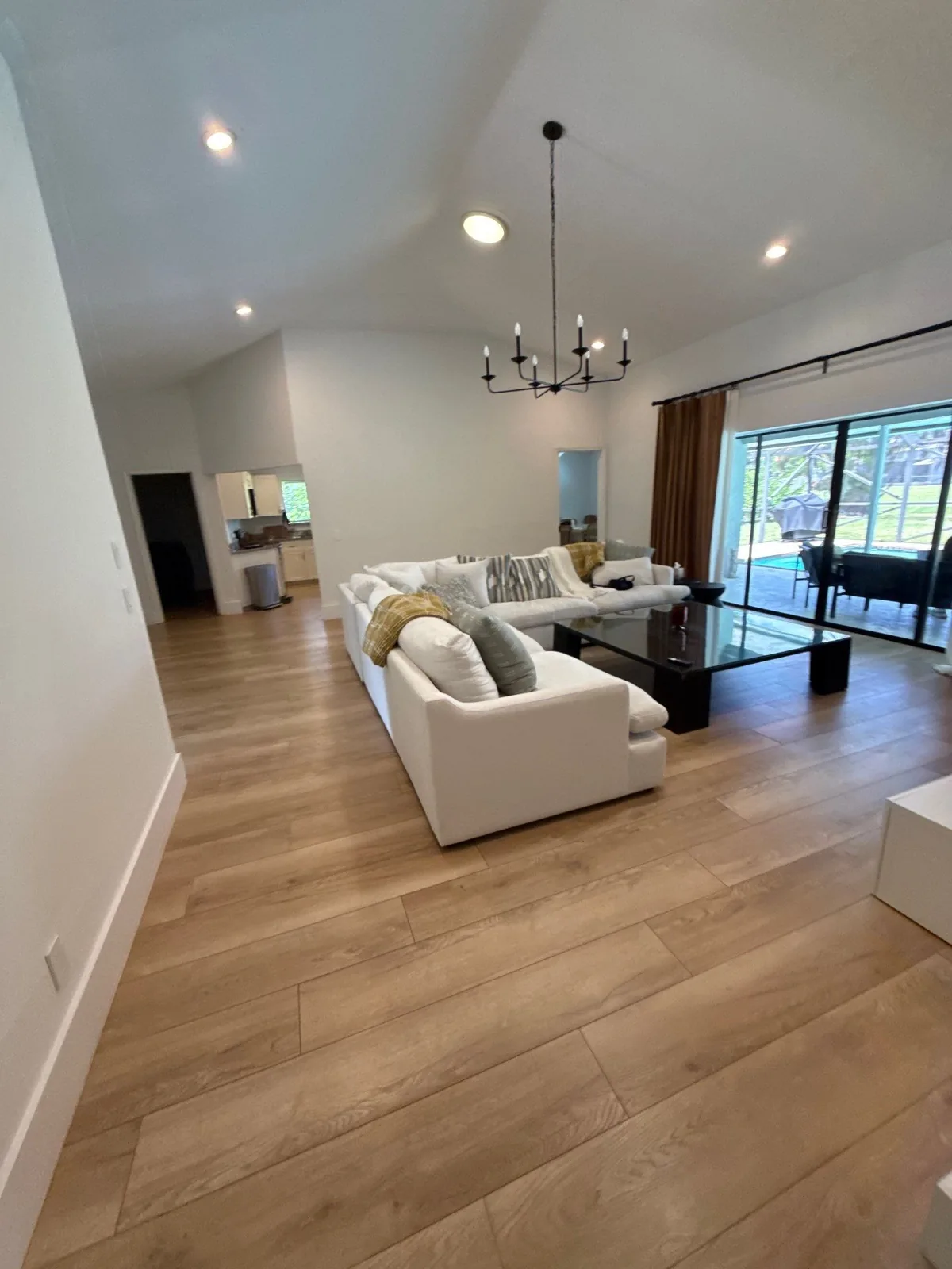 Interior Painting in Wellington, Florida. Large living room with vaulted white ceiling, white walls, black chandelier, white sectional sofa and sliding glass doors.