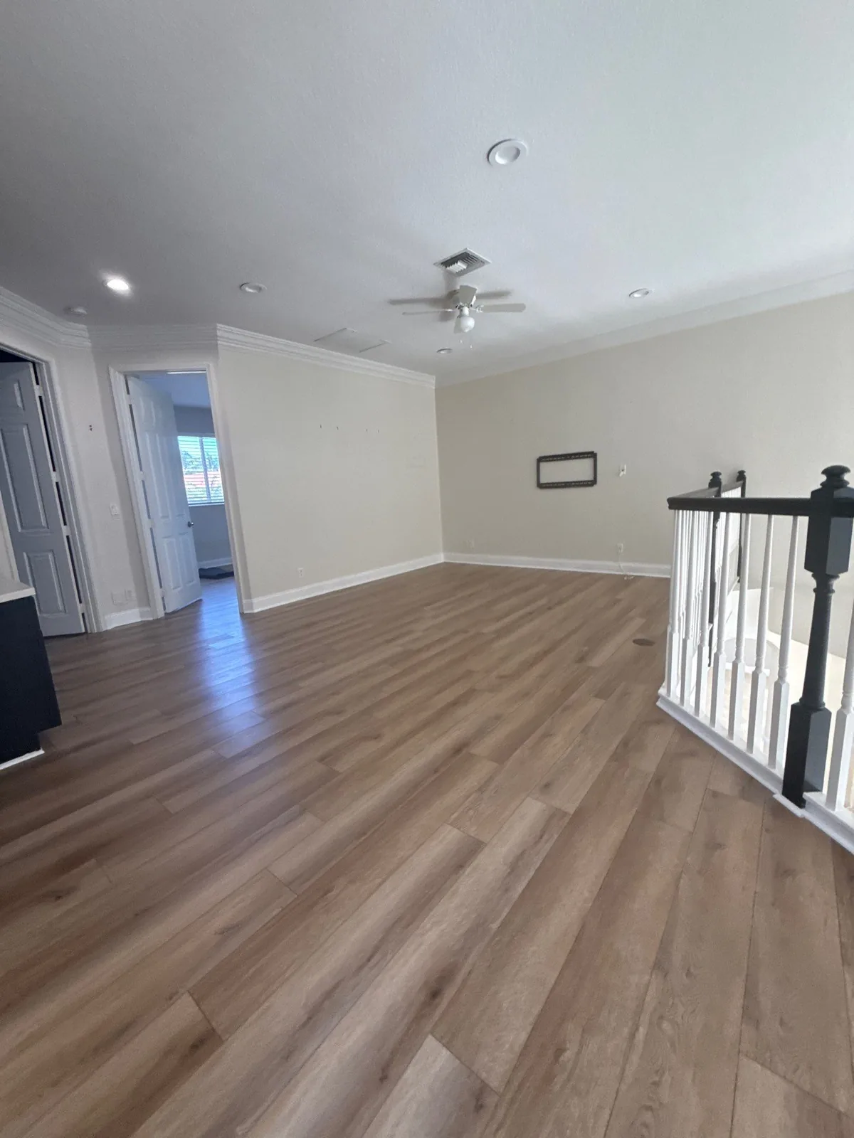 Interior Painting in Wellington, Florida. Empty living space with painted beige walls, white crown moulding and baseboards, wood-look plank flooring and a white stair railing.