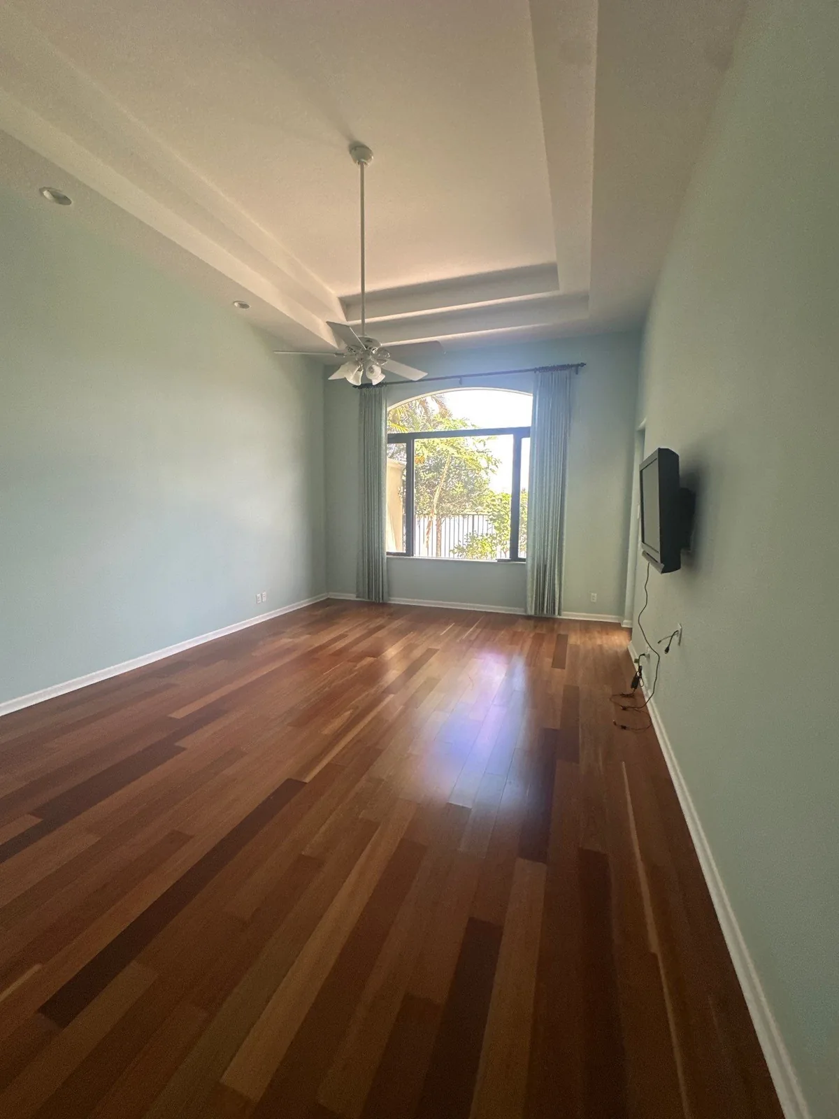 Interior Painting in Whisper Walk, Florida. Empty bedroom with pale blue-green walls, white stepped tray ceiling and dark wood floor.