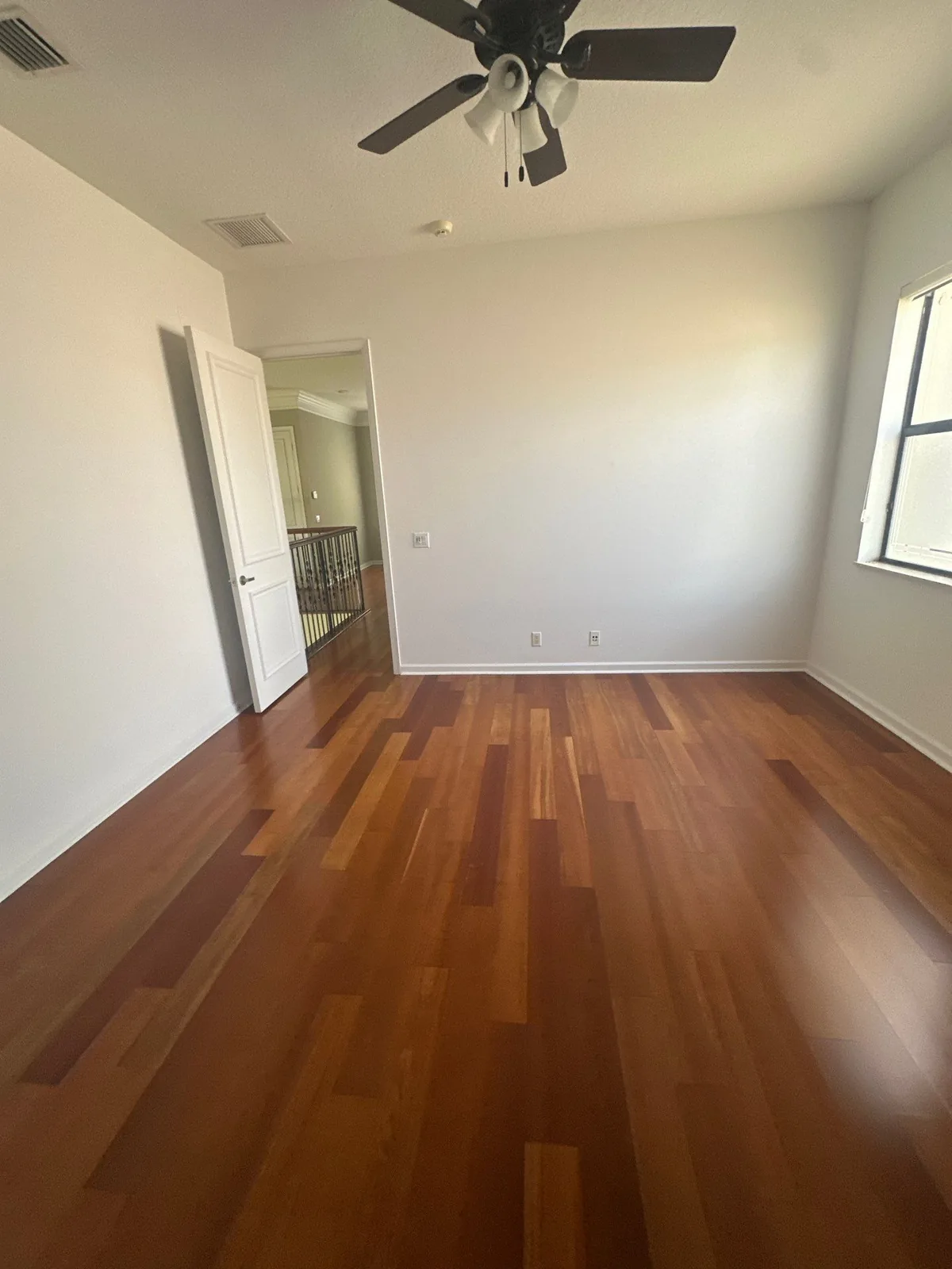 Interior Painting in Whisper Walk, Florida. Empty bedroom with freshly painted white walls and ceiling, white baseboards and door, dark hardwood floor and a ceiling fan.