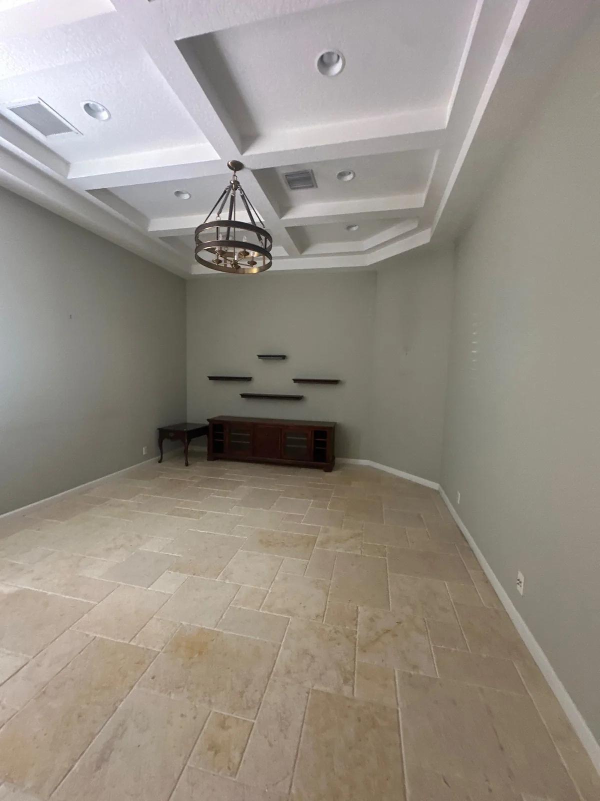 Interior Painting in Whisper Walk, Florida. Empty room with a white coffered ceiling, sage-grey painted walls, iron orb chandelier, floating shelves and travertine tile floor.