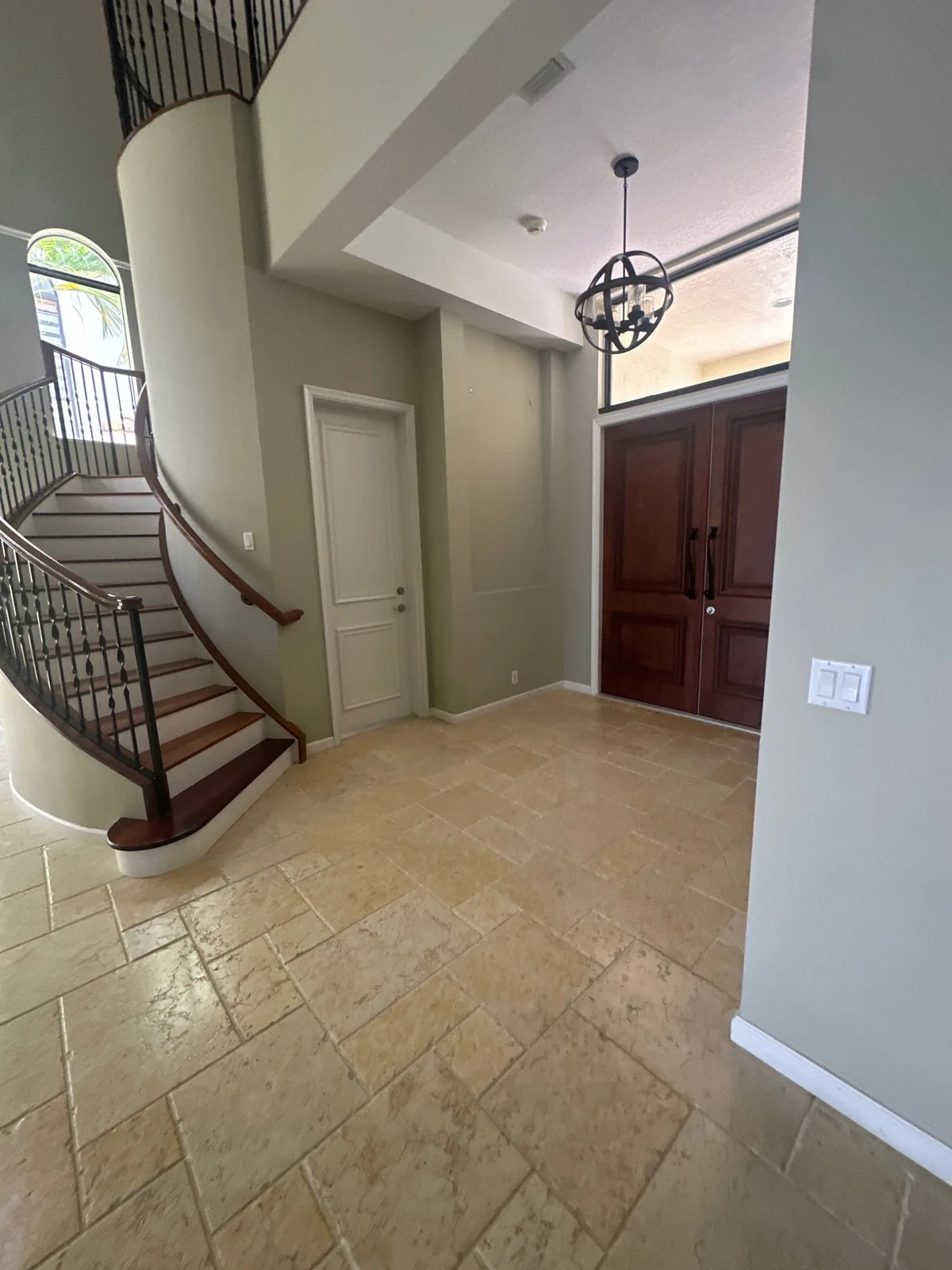 Interior Painting in Whisper Walk, Florida. Two-storey entry foyer with curved staircase and iron balusters, painted greige walls, white doors and trim, dark wood double entry doors.