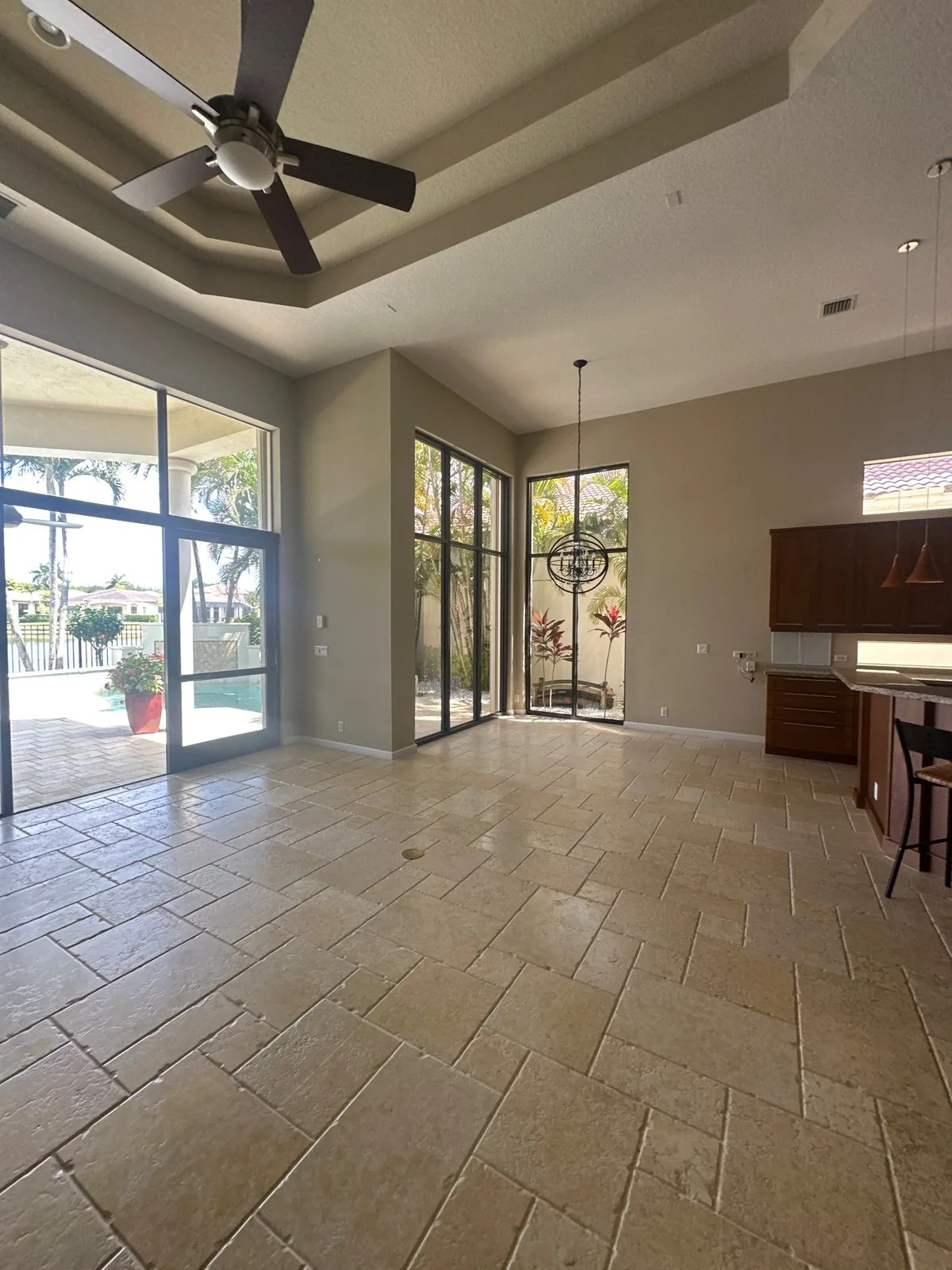 Interior Painting in Whisper Walk, Florida. Large empty living area with tray ceiling, painted walls, ceiling fan, sliding glass doors to a pool deck and travertine tile floor.